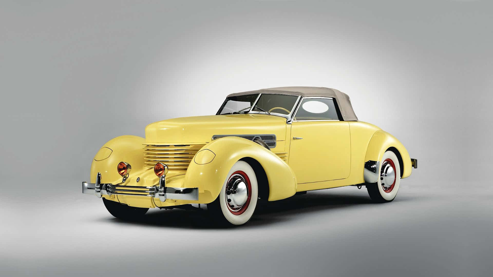 Beautiful Retro 桌布 壁紙 — 一輛復古黃色敞篷車，帶有鍍鉻裝飾和白色輪胎，擺放在中性灰色工作室背景前。