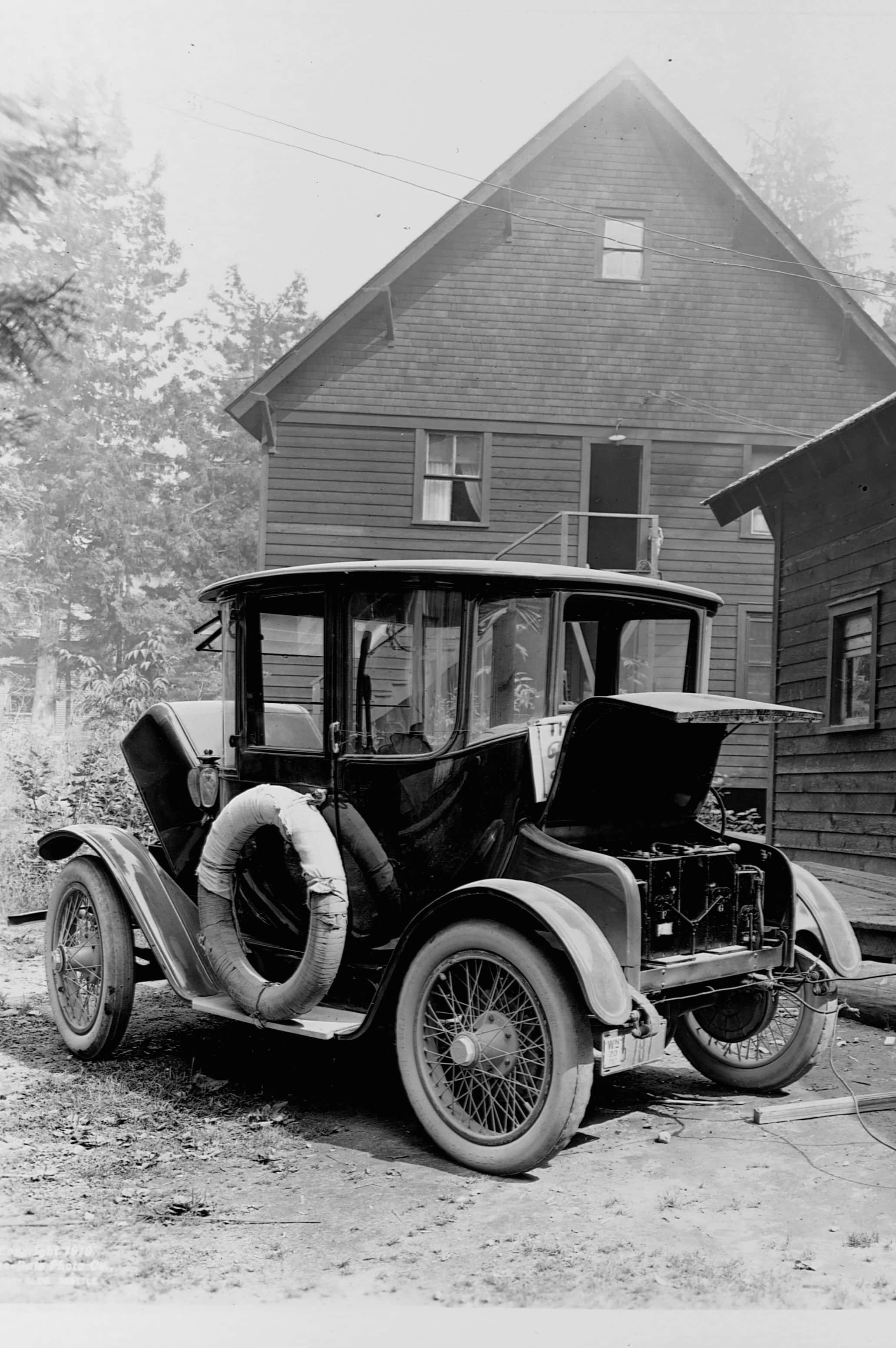 Black And White Vintage Car 桌布 壁紙 — 一輛復古黑色汽車，引擎蓋打開，備用輪胎，停在一間被樹木環繞的木屋前。