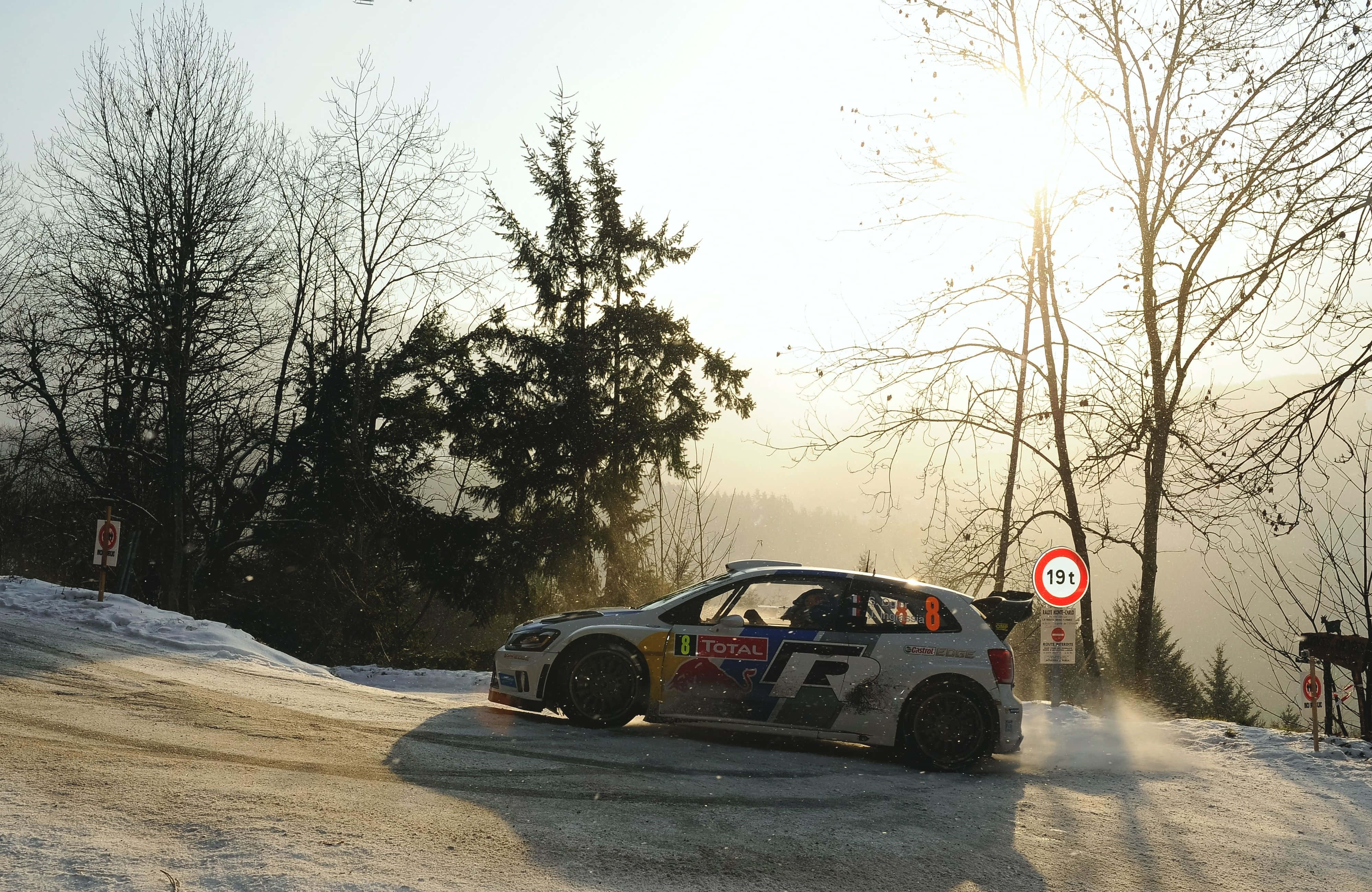 Ice Racing 桌布 壁紙 — 一輛拉力賽車在日出時分飛馳在積雪的森林道路上，背景是光禿的樹木和霧氣繚繞的山丘。