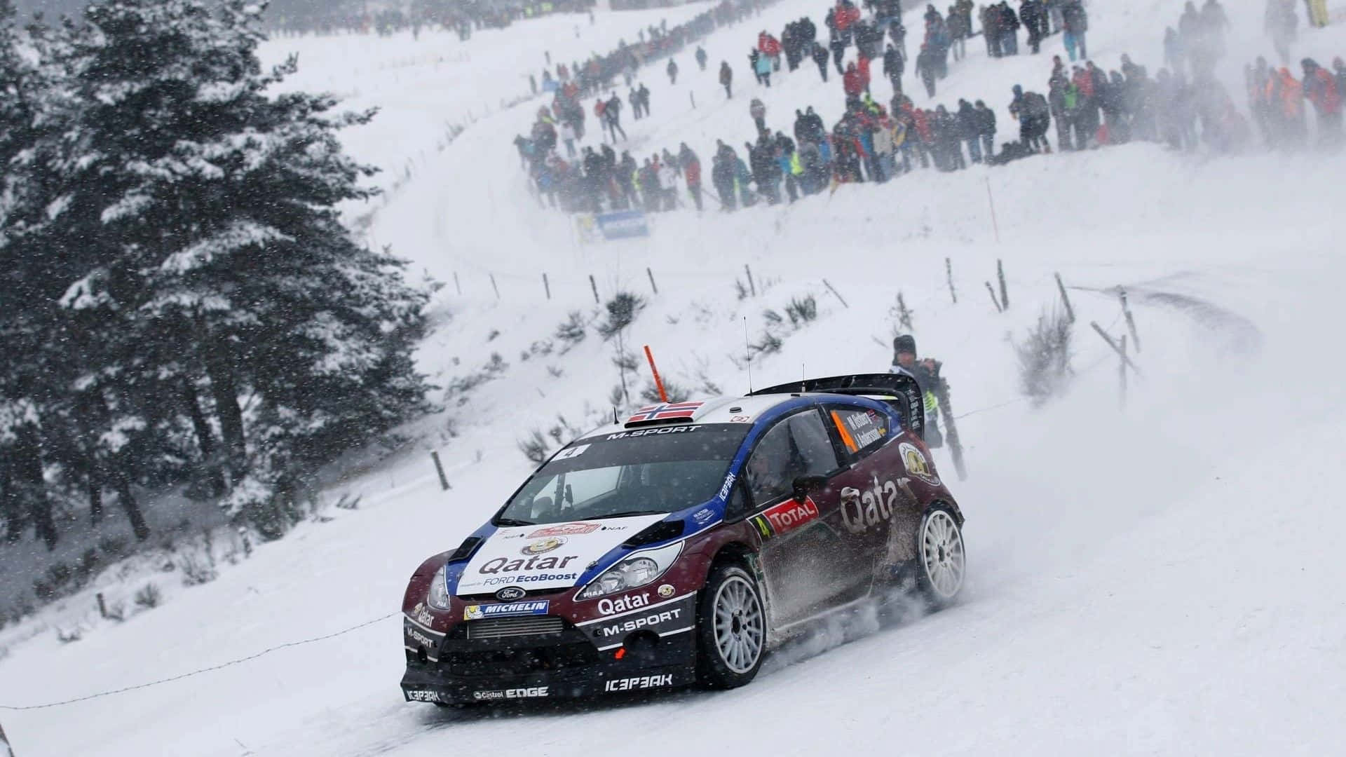 Ice Racing 桌布 壁紙 — 一輛拉力賽車在白雪覆蓋的山口疾馳，揚起雪花，觀眾在積雪的山坡上觀看。