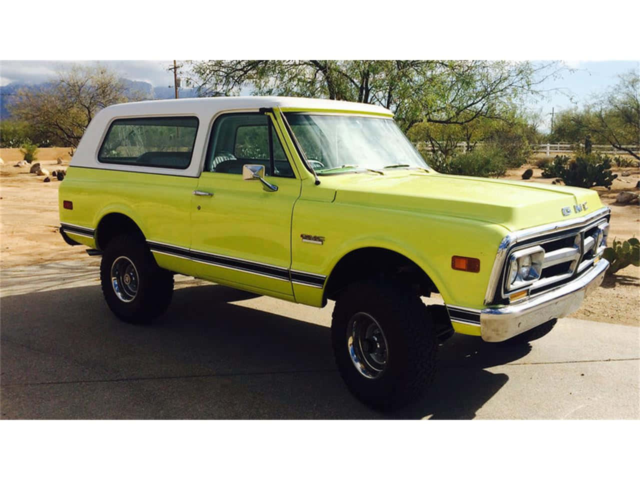 Gmc Jimmy 桌布 壁紙 — 一輛明亮的青檸綠色經典雪佛蘭K5 Blazer，白色車頂，停在鋪砌的車道上，背景是沙漠景觀，有仙人掌和遠處的山脈，天空清澈湛藍。