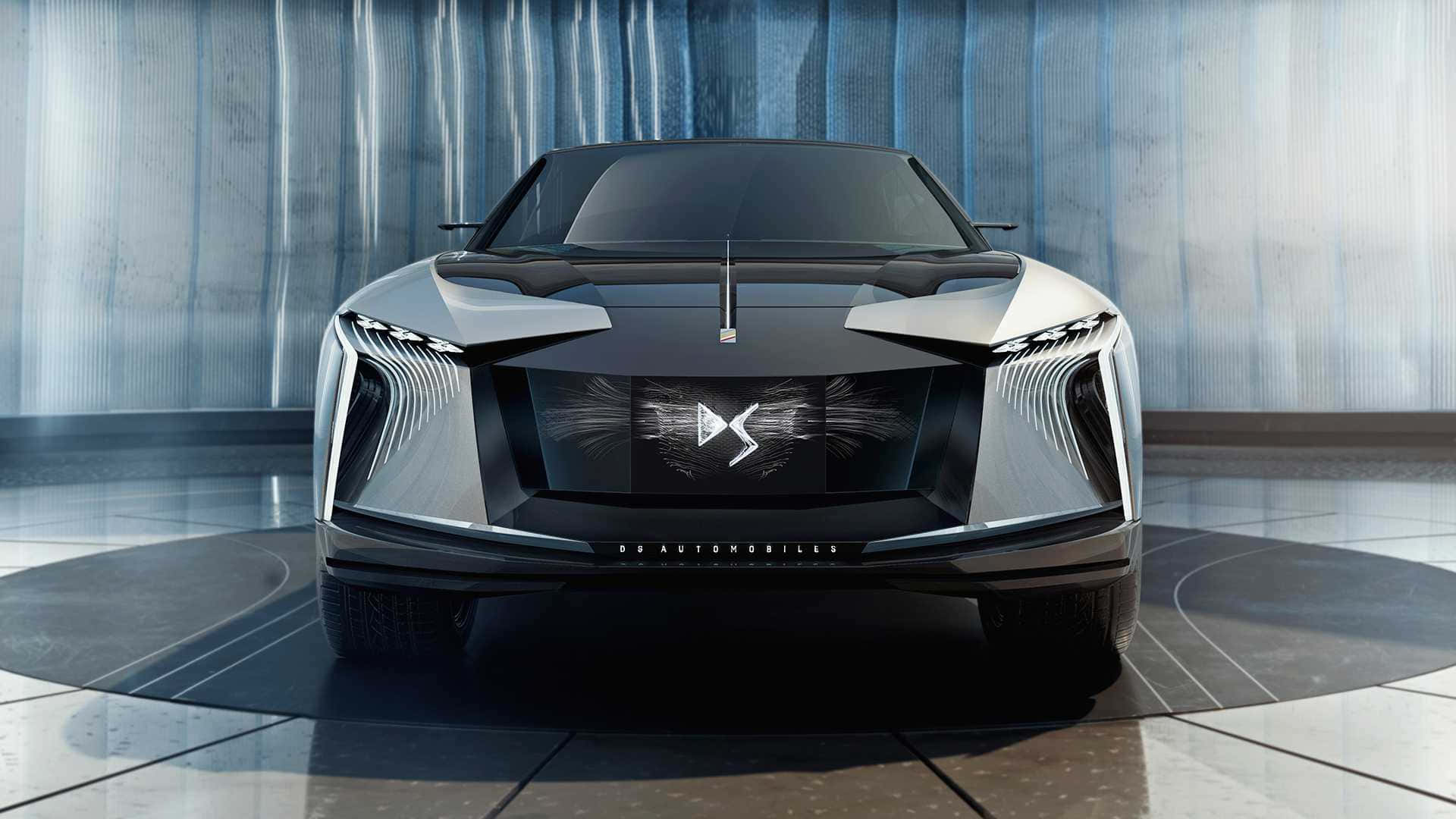 Ds Automobiles 桌布 壁紙 — 一輛時尚未來感十足的銀色跑車，配備銳利角形頭燈和發光標誌，在垂直藍色燈光下居中放置於拋光地板上。