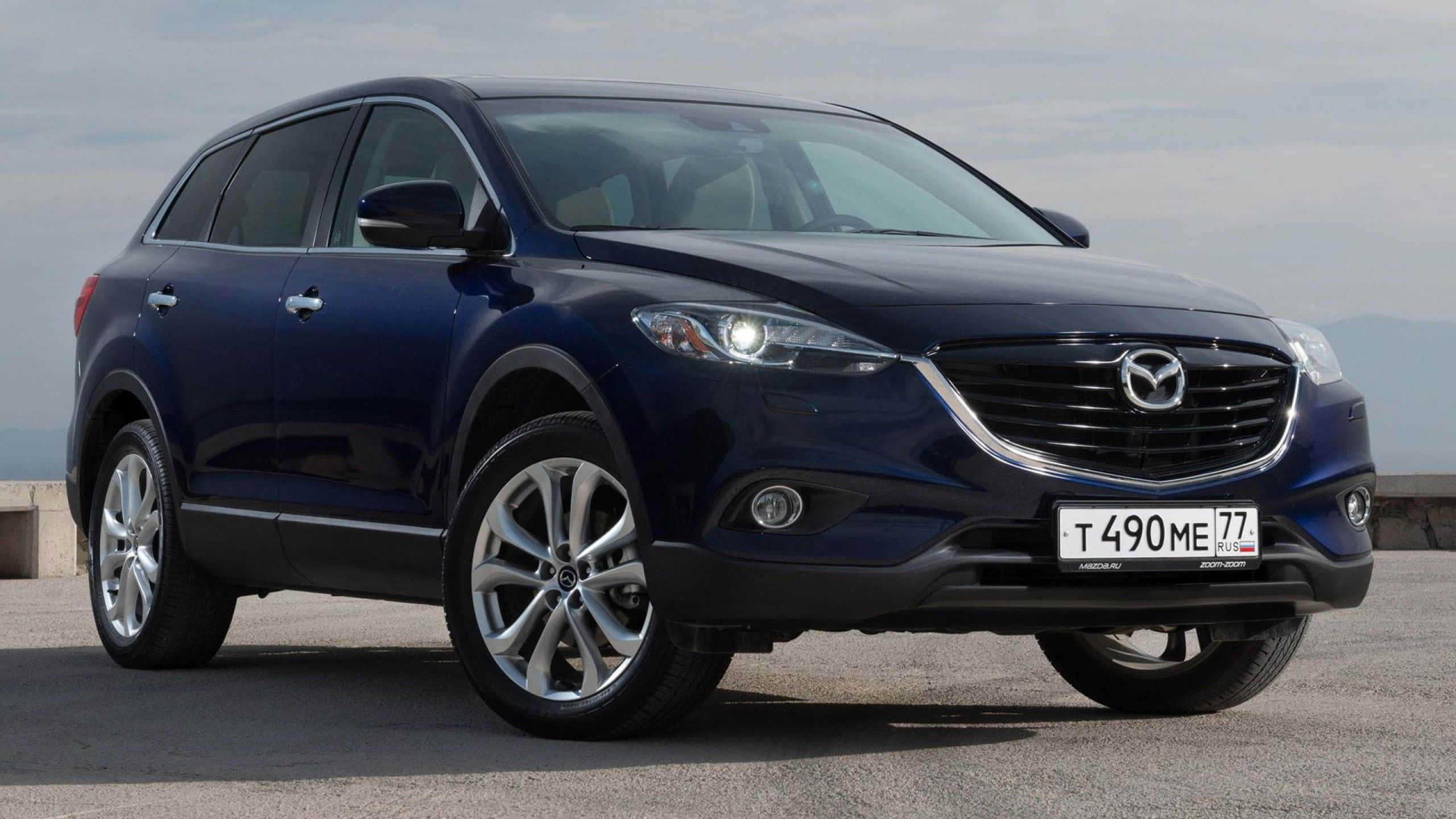 Mazda Cx-9 桌布 壁紙 — 一輛時尚深藍色Mazda CX-9 SUV停泊在混凝土表面上，遠山在陰天天空下。