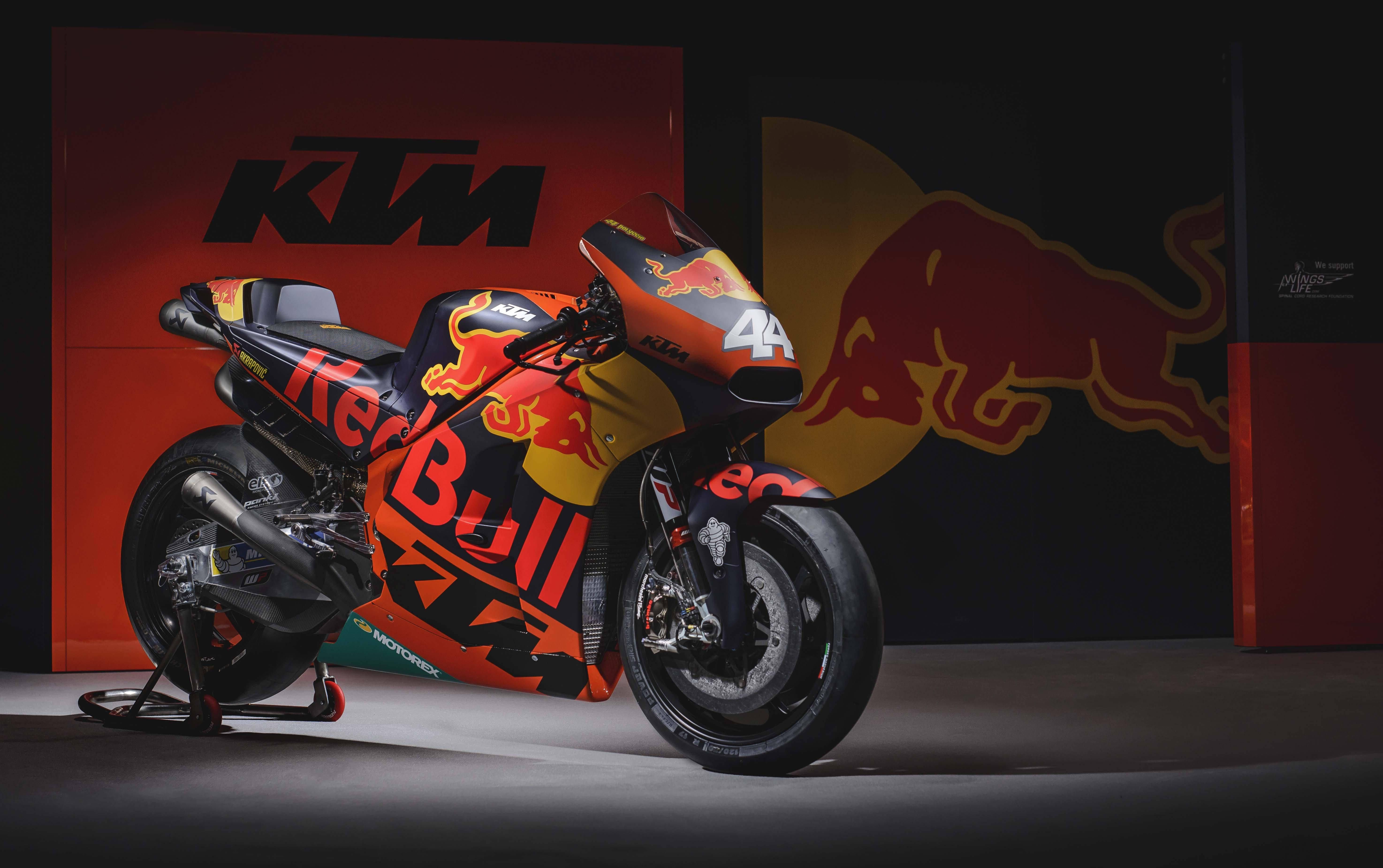機車 桌布 壁紙 — 一輛時尚的KTM Red Bull賽車摩托車，編號44，在帶有品牌標誌的背景下，以強烈的紅色和黑色色調戲劇性地照亮。