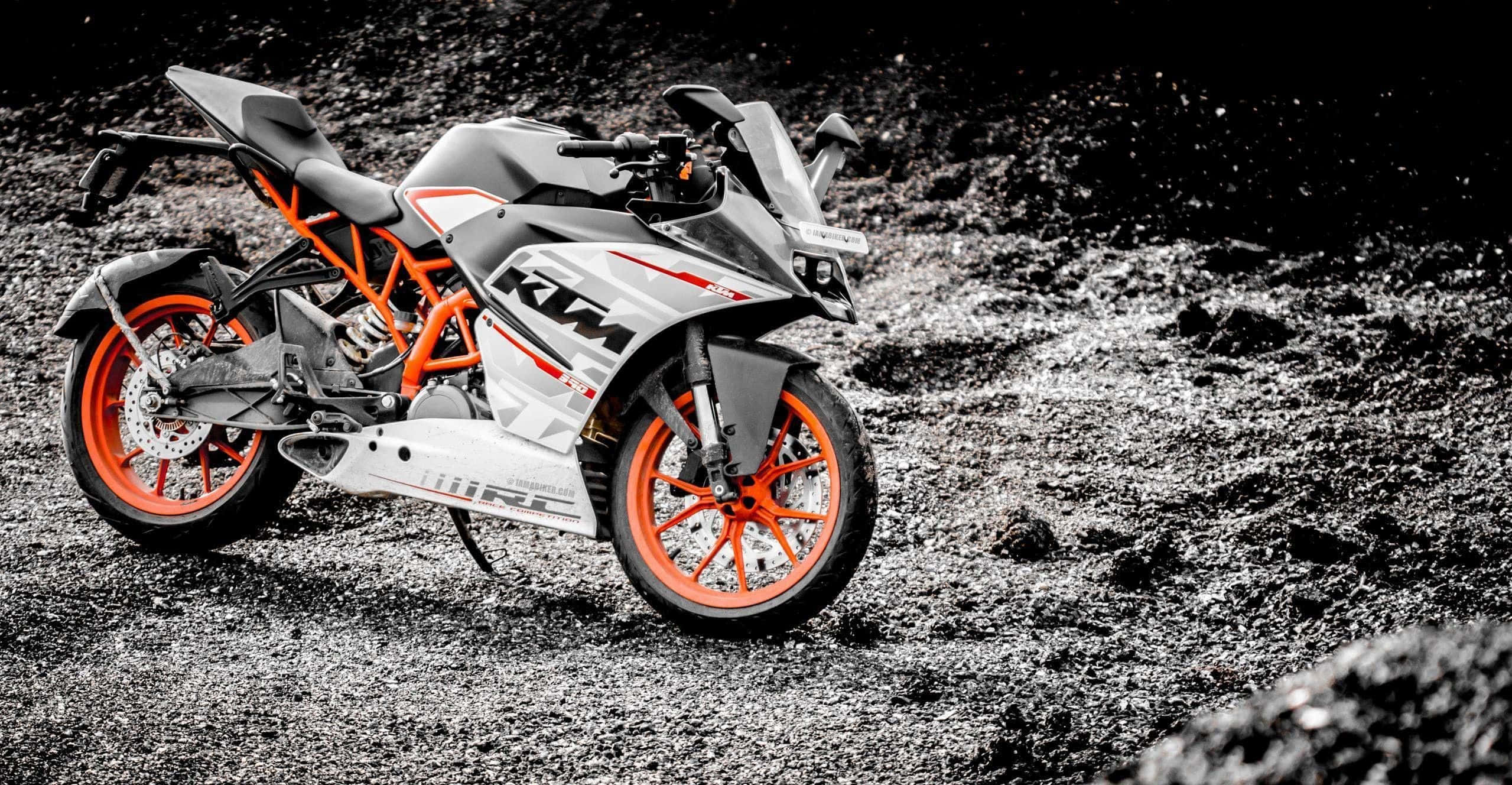 Ktm Bike 桌布 壁紙 — 一輛時尚的KTM電單車，配以鮮艷的橙色車輪，在強烈黑白對比燈光下，立於碎石地面上。