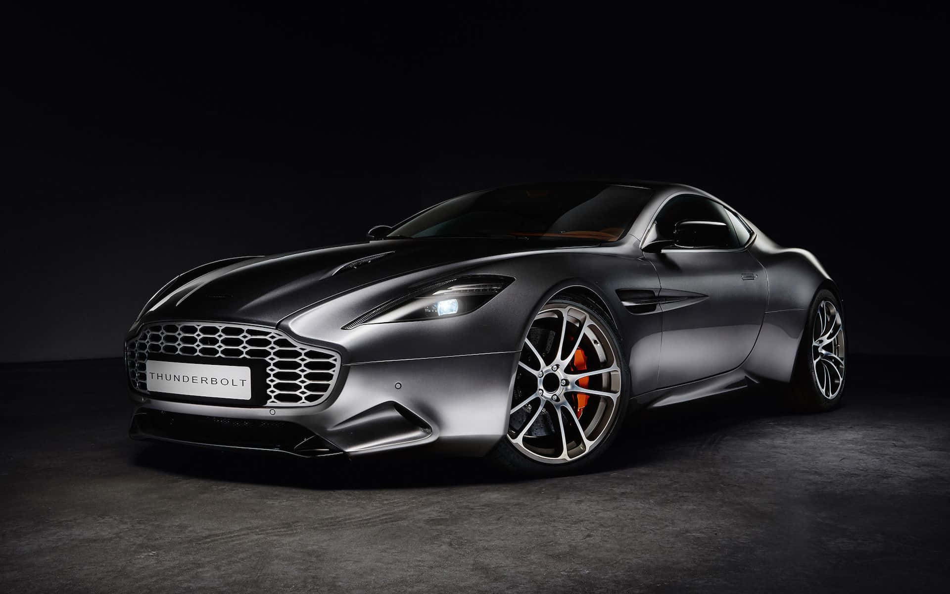 Aston Martin Vanquish 桌布 壁紙 — 一輛時尚的啞光灰色 Aston Martin Thunderbolt 跑車在黑暗背景下於工作室燈光下閃耀。
