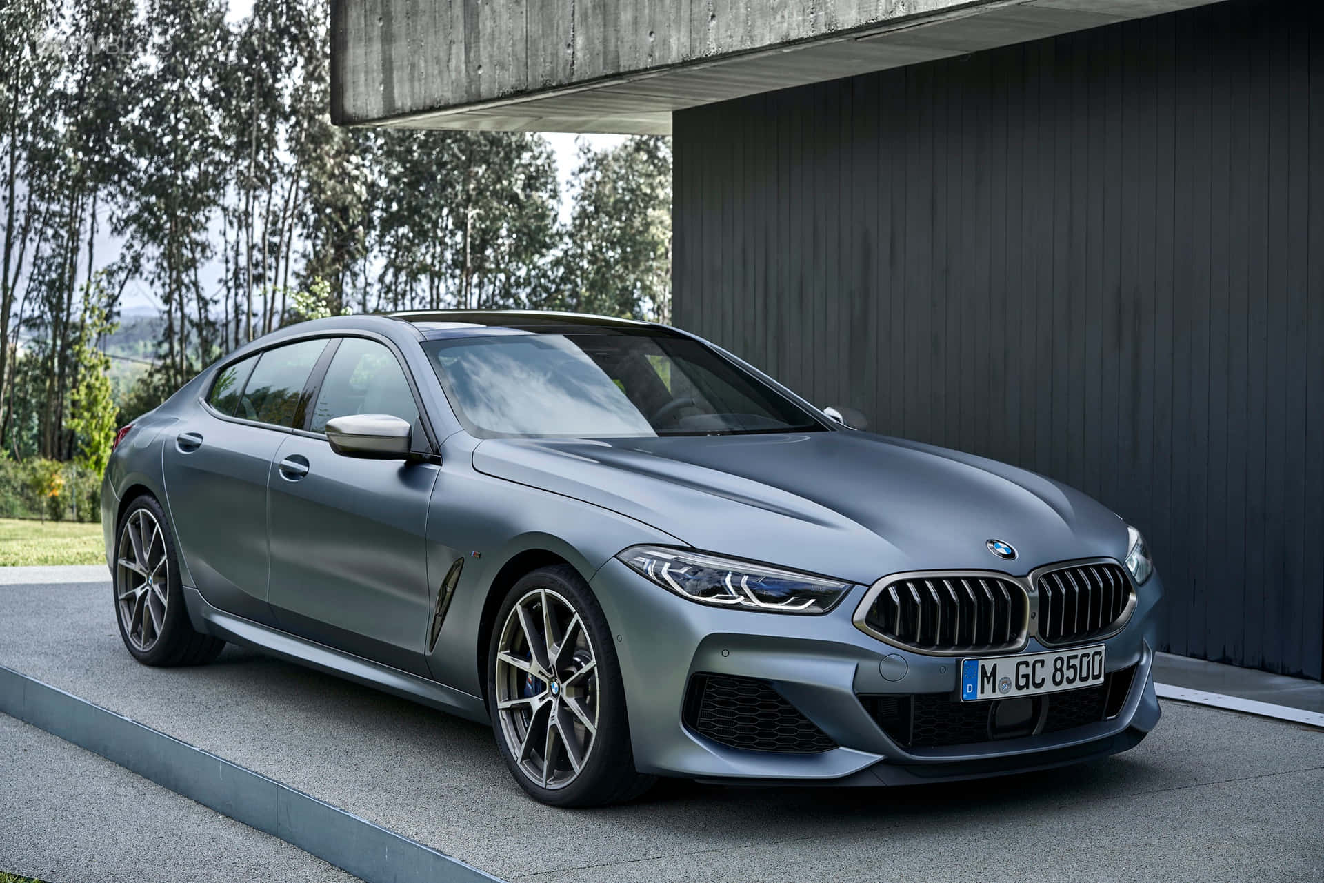 Bmw 8 Series 桌布 壁紙 — 一輛時尚的啞光灰色BMW 8系轎跑車停在現代混凝土懸挑下，背景有樹木。