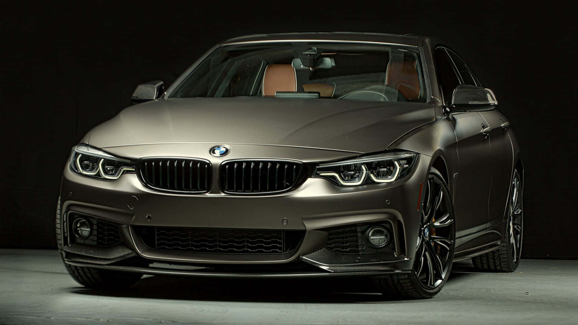 Bmw 4 Series 桌布 壁紙 — 一輛時尚的啞光灰色BMW轎車，配備黑色輪圈和發光頭燈，在深色工作室背景下展示。