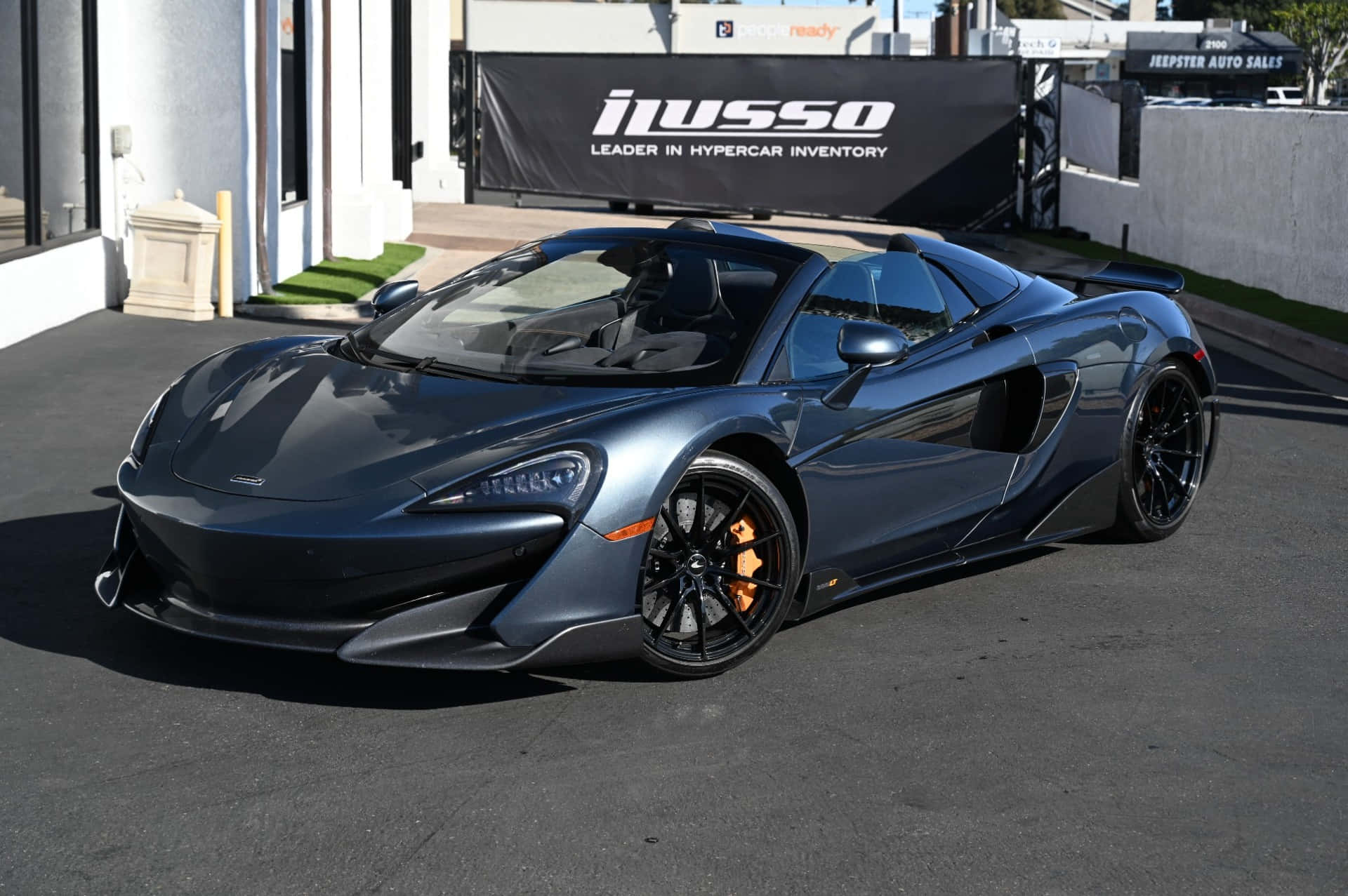 Mclaren 600lt Spider 桌布 壁紙 — 一輛時尚的啞光灰色McLaren 570S跑車停在經銷商前的瀝青路面上，經銷商掛有黑色橫幅。