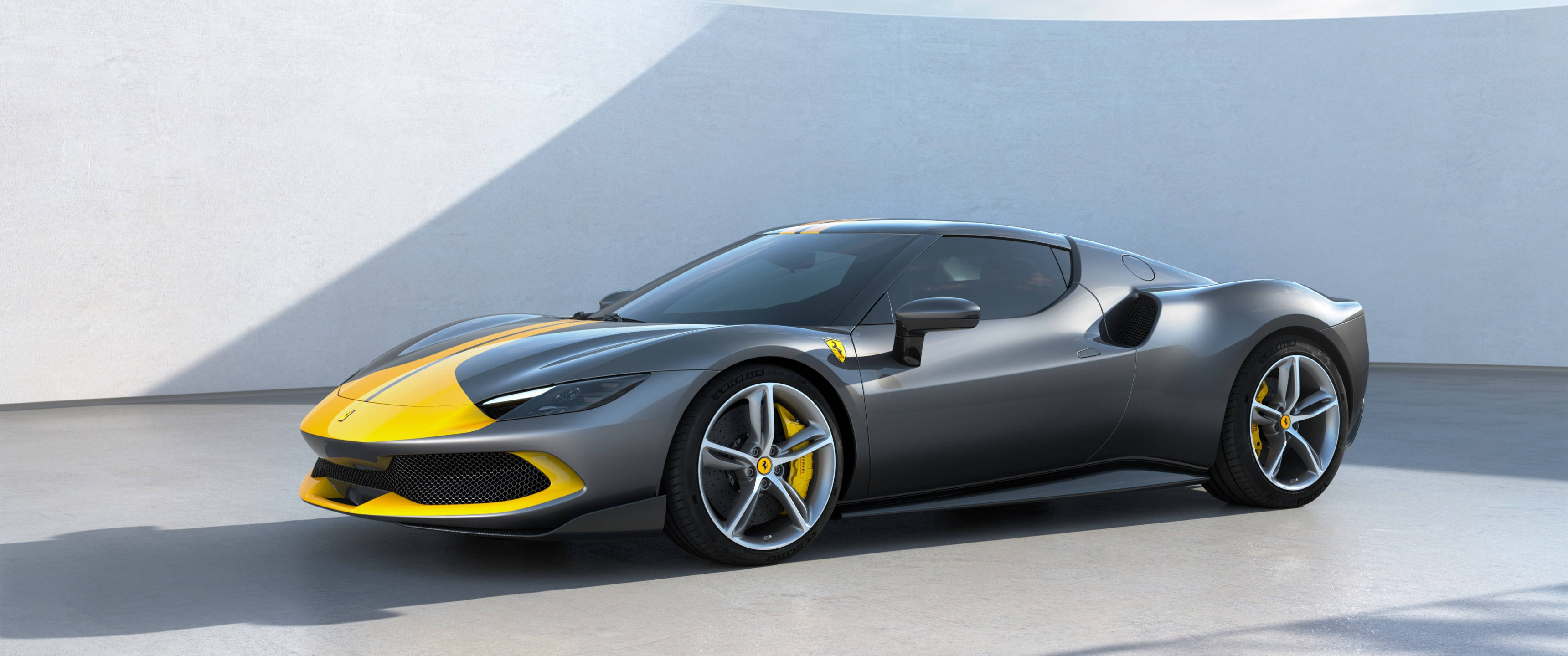 Sports Car 桌布 壁紙 — 一輛時尚的啞光灰色法拉利跑車，帶有醒目的黃色點綴，在明亮的日光下停在極簡主義的混凝土牆前。