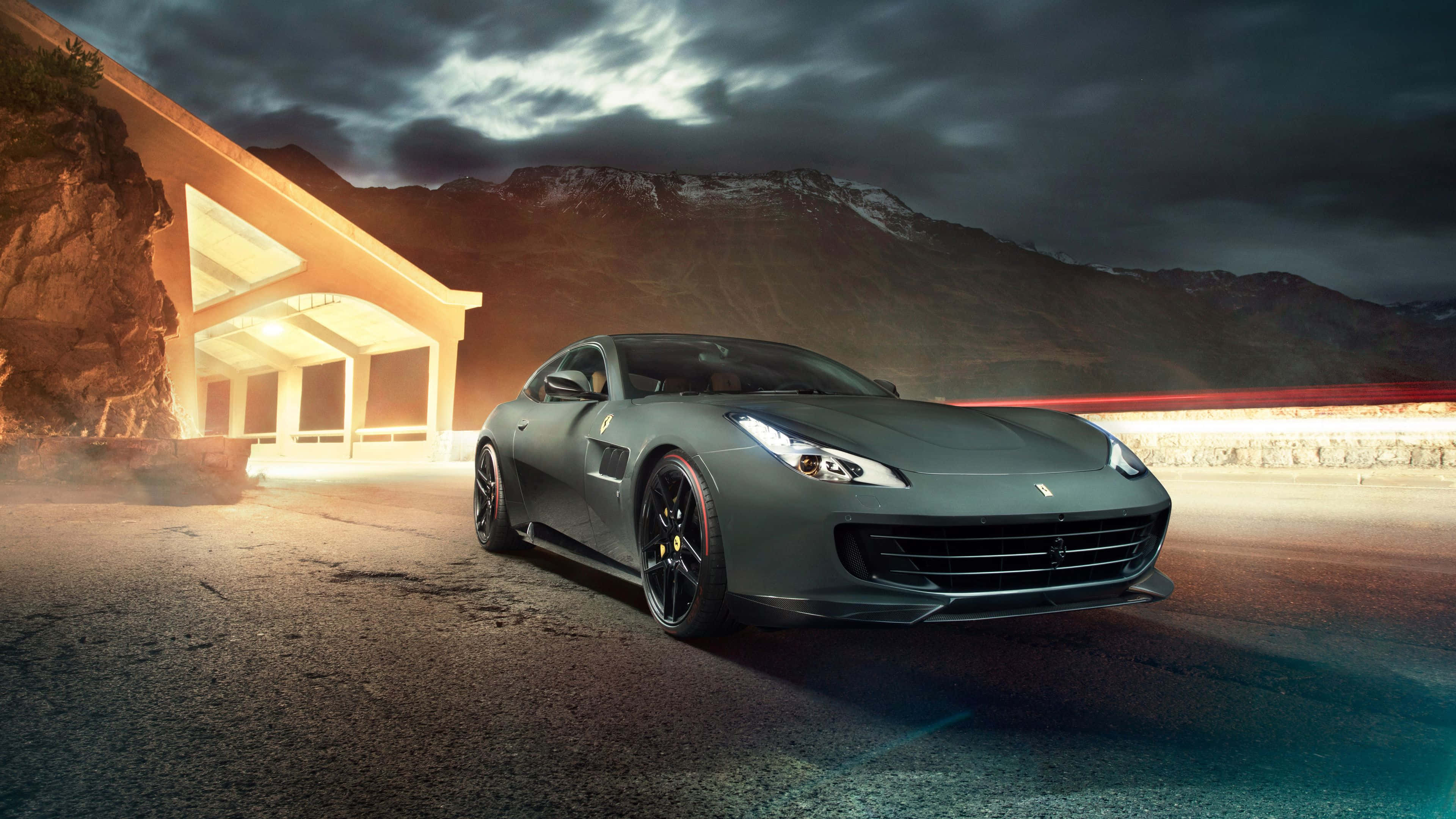 Ferrari Gtc4lusso 桌布 壁紙 — 一輛時尚的啞光灰色法拉利跑車在戲劇性的暮色天空下滑行，背景是白雪覆蓋的山脈。