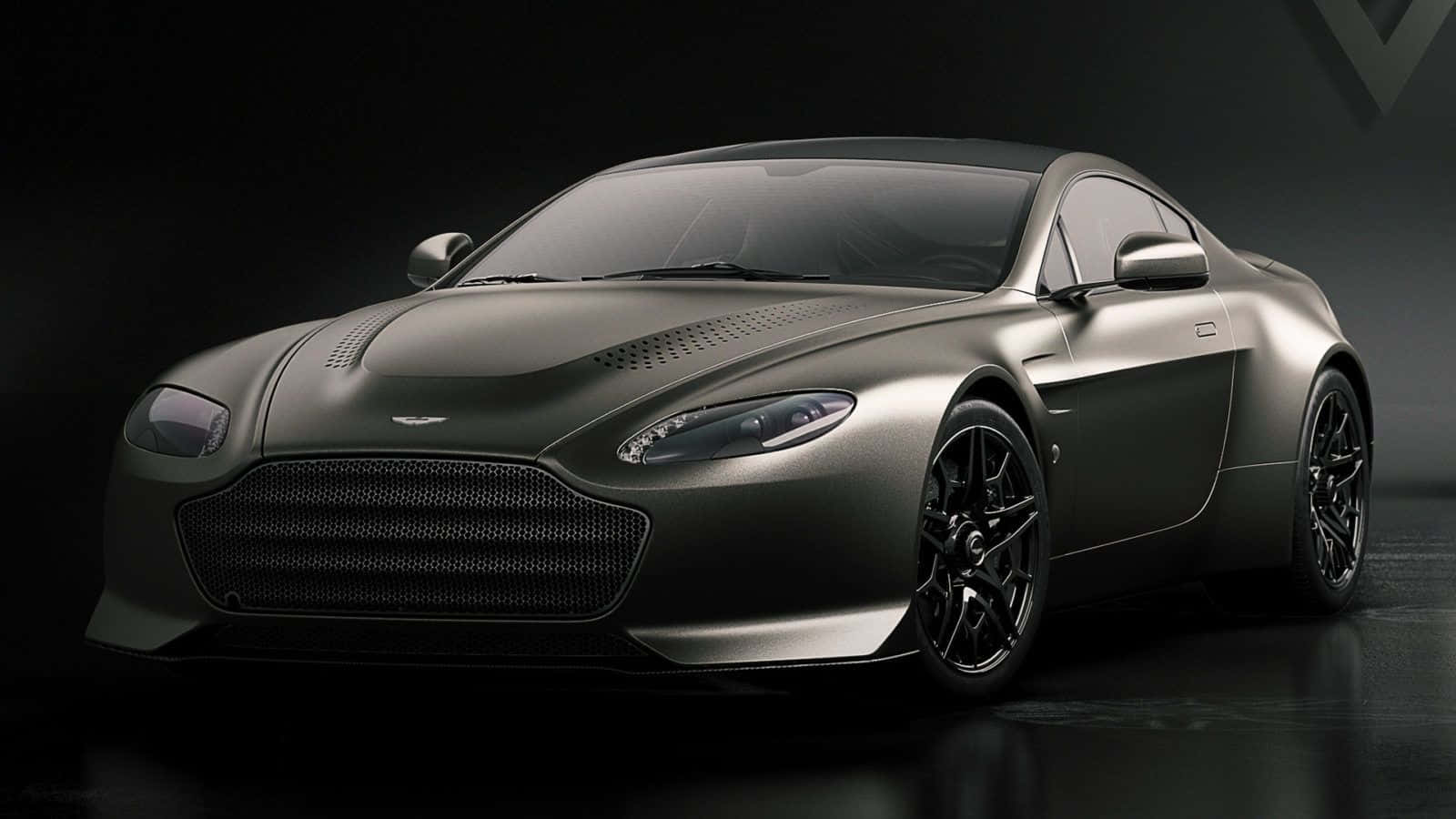 Aston Martin V12 Vantage 桌布 壁紙 — 一輛時尚的啞光灰色阿斯頓馬丁跑車在戲劇性的工作室燈光下，在深色背景中閃耀。