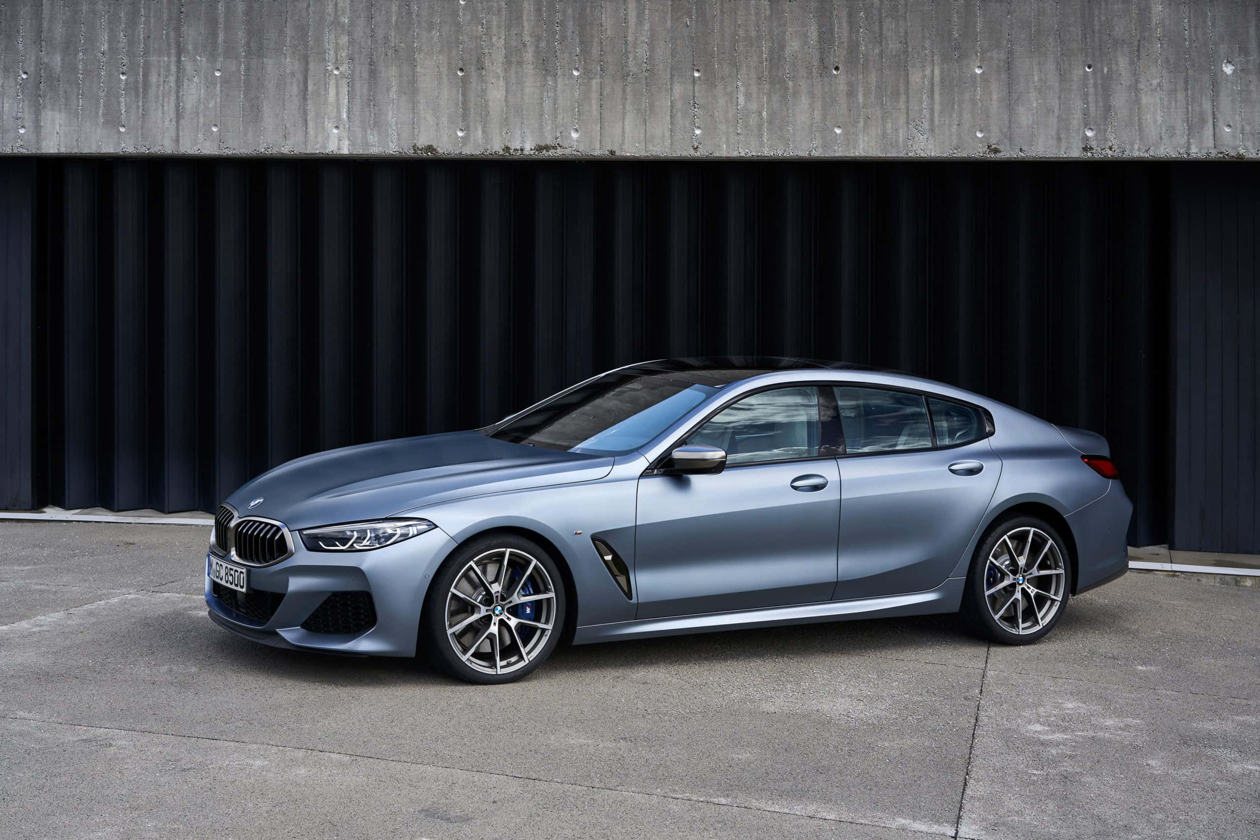 Bmw 8 Series 桌布 壁紙 — 一輛時尚的啞光藍色BMW 8系轎跑車停放在現代混凝土和深色金屬牆前。