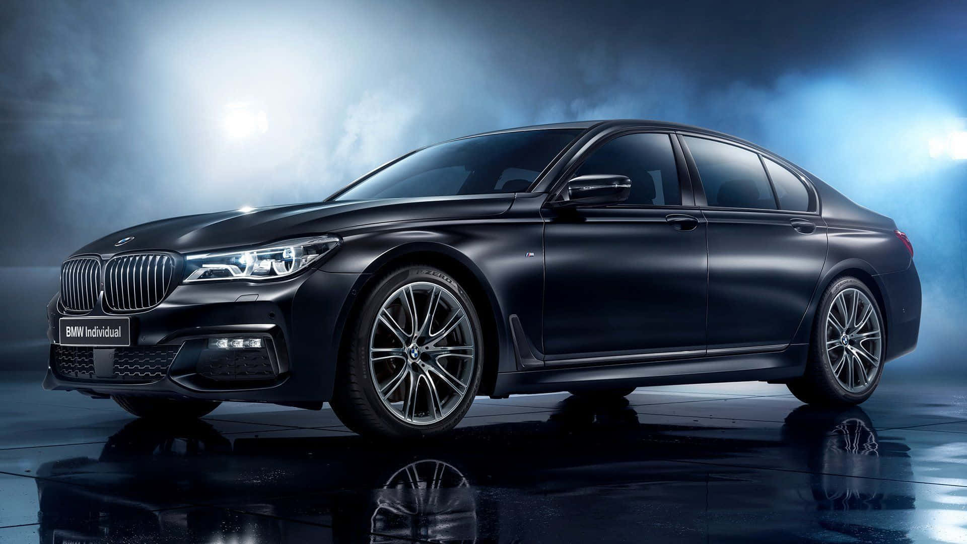 Bmw 7 Series 桌布 壁紙 — 一輛時尚的啞光黑色BMW Individual轎車在戲劇性的工作室燈光下，配合藍色煙霧和反光的濕地板閃耀。