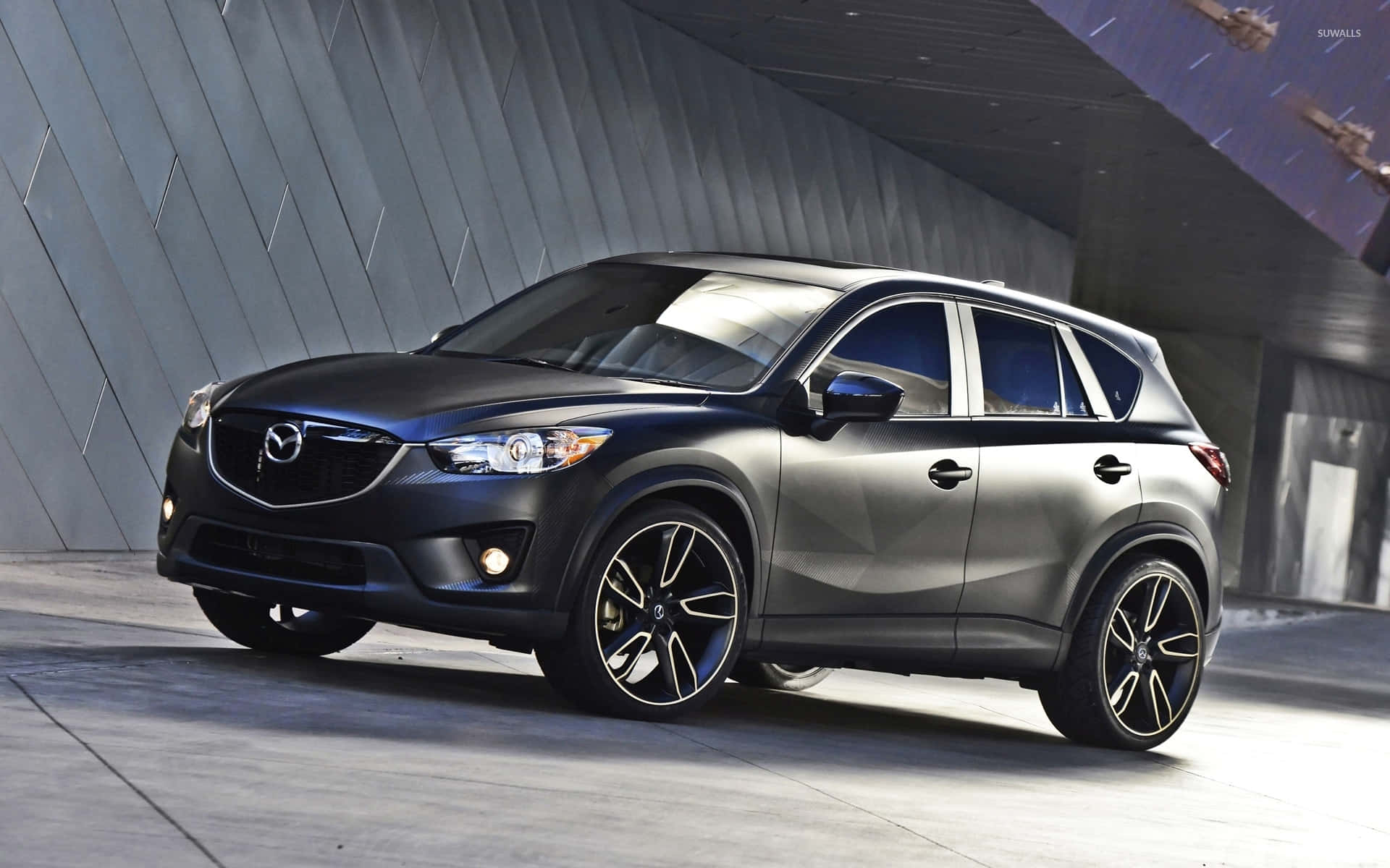 Mazda Cx-5 桌布 壁紙 — 一輛時尚的啞光黑色萬事得 CX-5 SUV 配備黑色輪圈，停放在現代角形混凝土結構下。