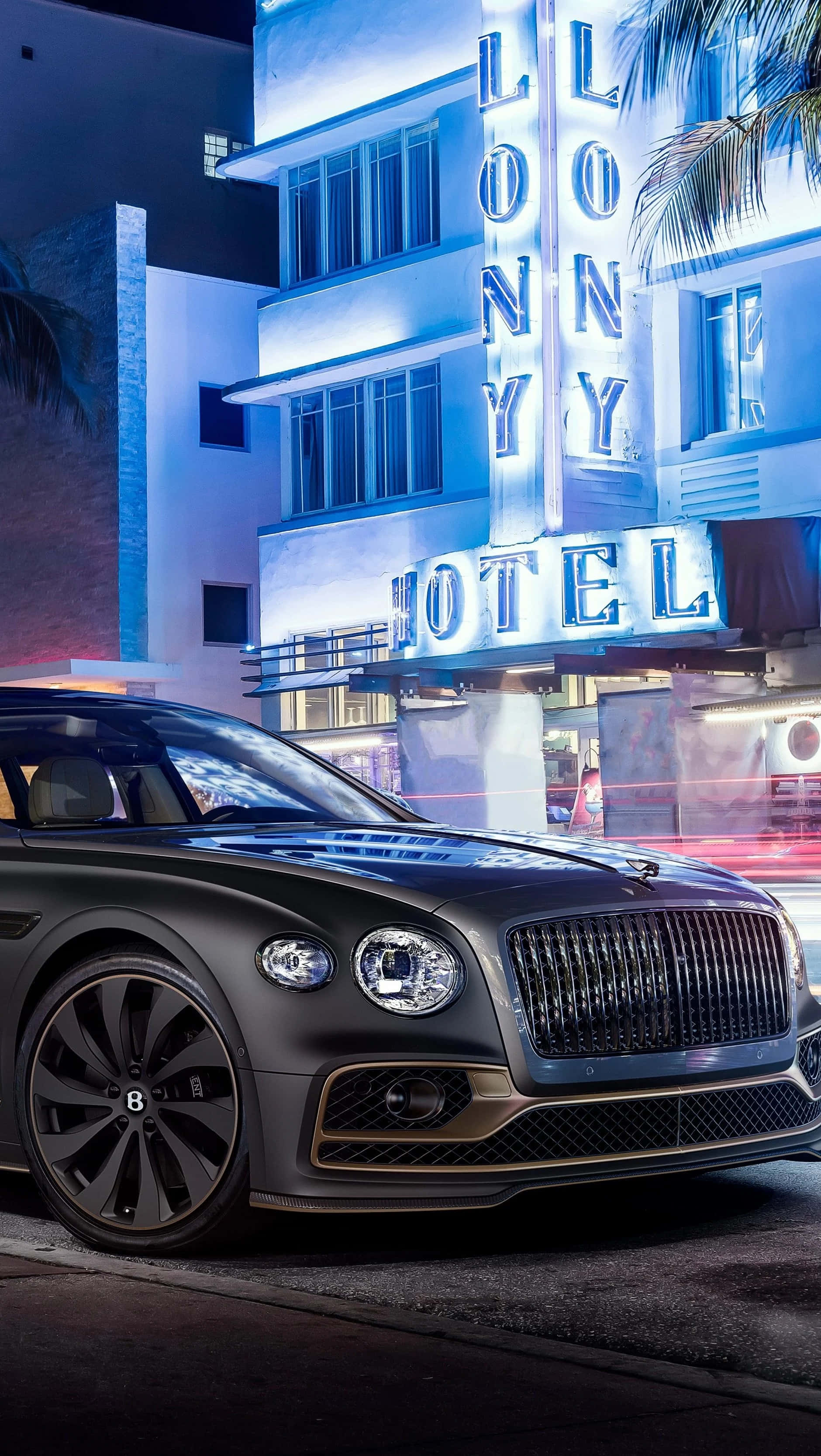 Bentley Flying Spur 桌布 壁紙 — 一輛時尚的啞光黑色賓利在夜間停泊在發光的霓虹燈 'LONNY HOTEL' 標誌和棕櫚樹前。
