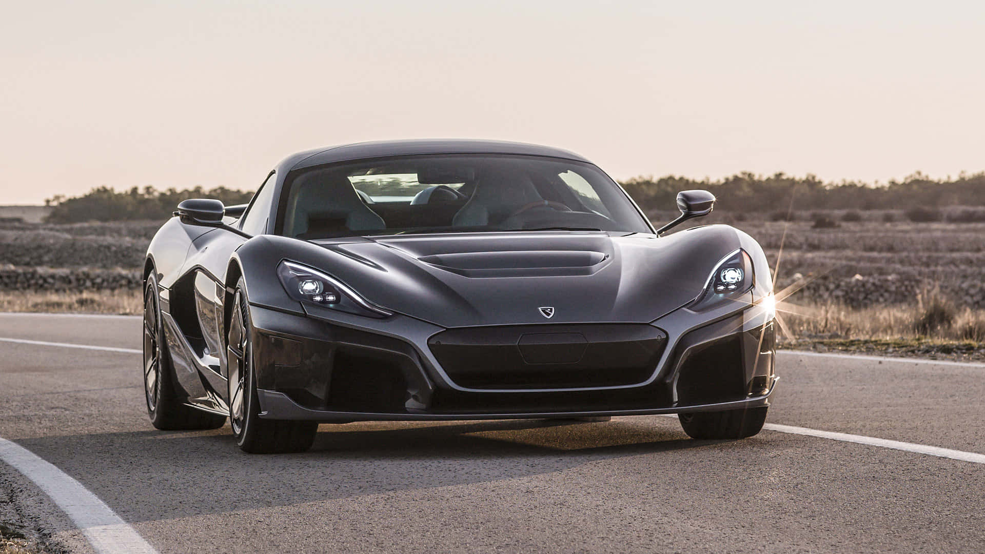 Rimac 桌布 壁紙 — 一輛時尚的啞光黑色跑車，車頭燈閃爍，在黃金時段行駛在沙漠公路上。