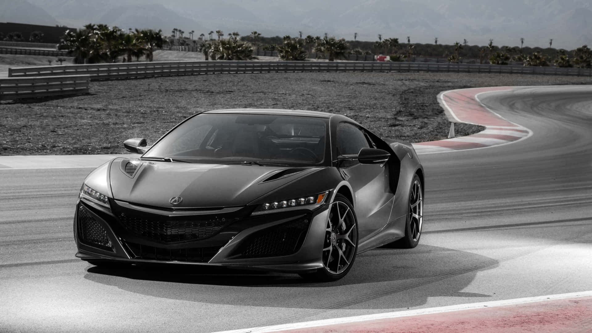 Acura Nsx 桌布 壁紙 — 一輛時尚的啞光黑色跑車在彎曲的賽道上飛馳，背景有棕櫚樹和山脈。