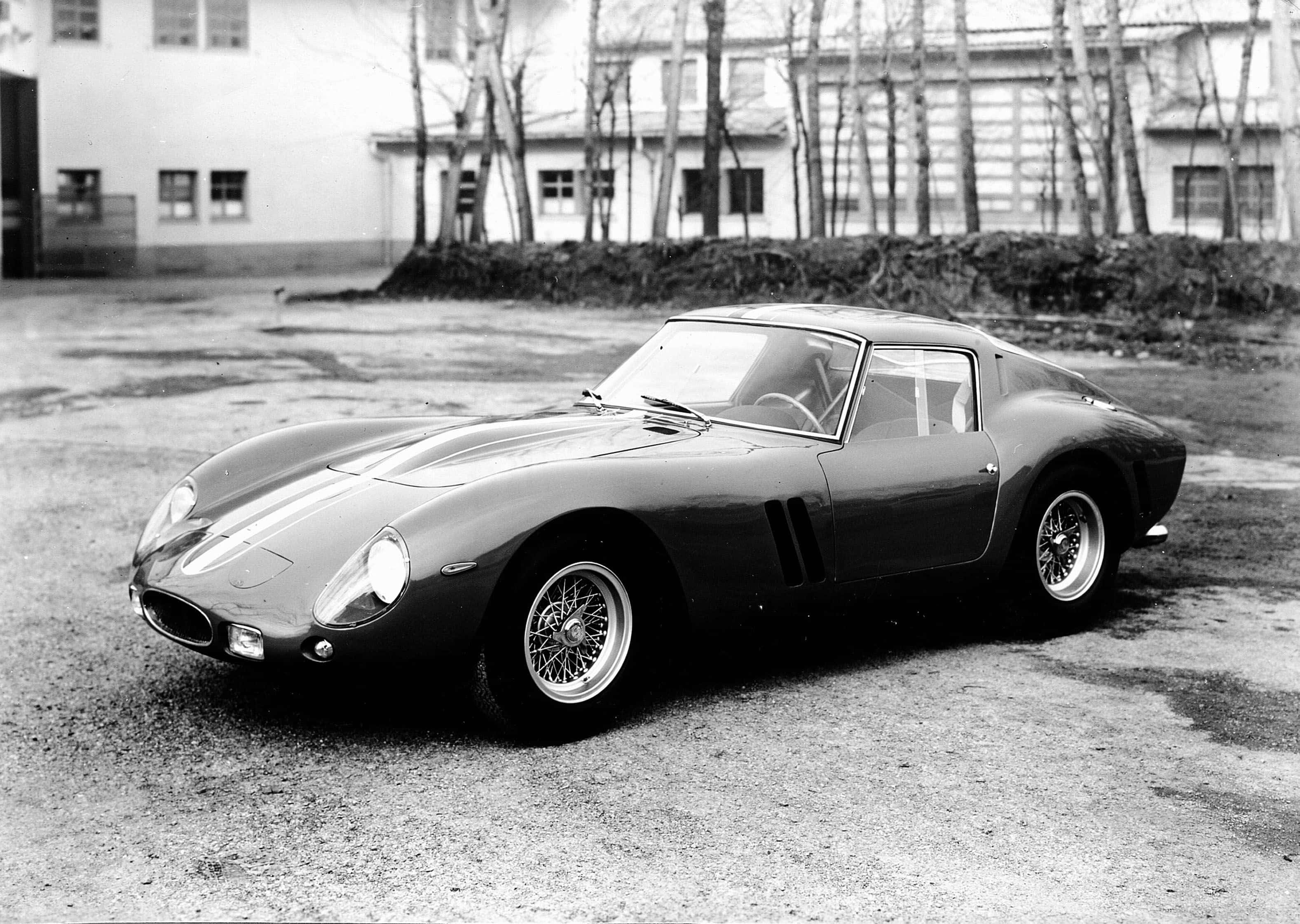 Black And White Vintage Car 桌布 壁紙 — 一輛時尚的復古法拉利250 GTO停泊在建築物前的碎石地上，背景有光禿禿的樹木。