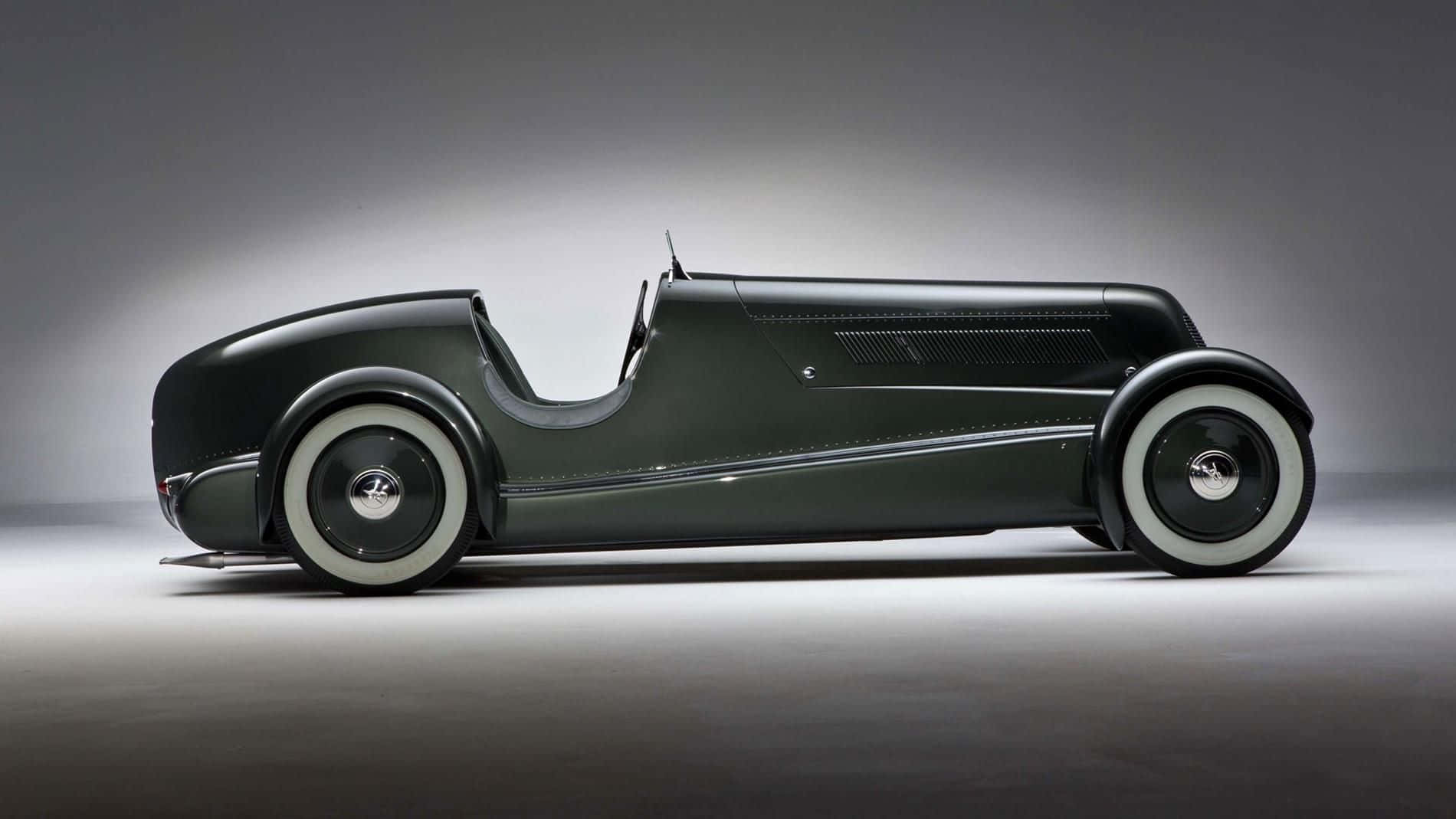 Car Design 桌布 壁紙 — 一輛時尚的復古賽車，採用磨砂深綠色車身和白色側壁輪胎，在極簡灰色工作室背景前蓄勢待發。
