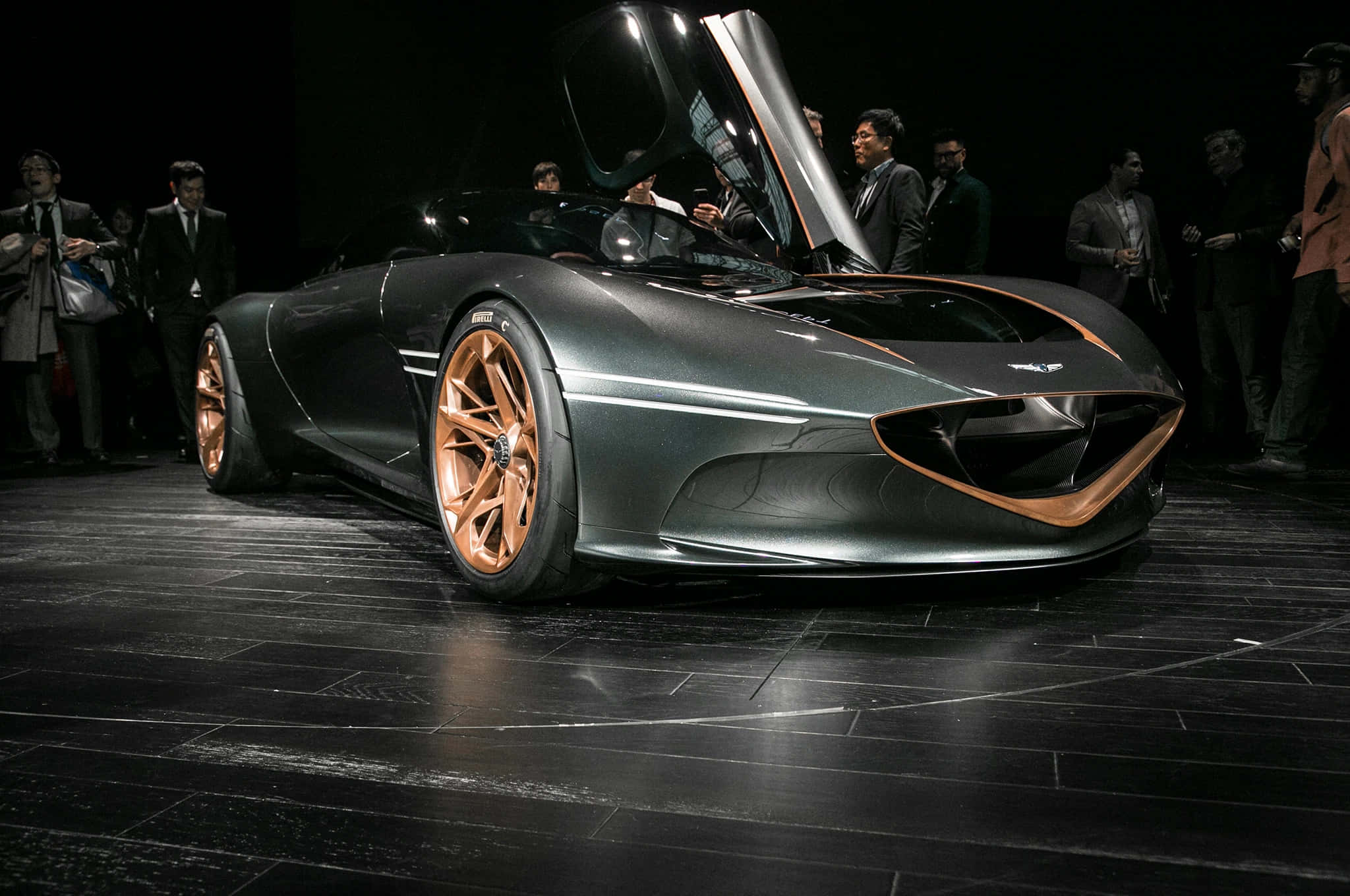 Genesis Essentia 桌布 壁紙 — 一輛時尚的未來主義跑車，帶有銅色點綴和打開的鷗翼門，在戲劇性的舞台燈光下展示。
