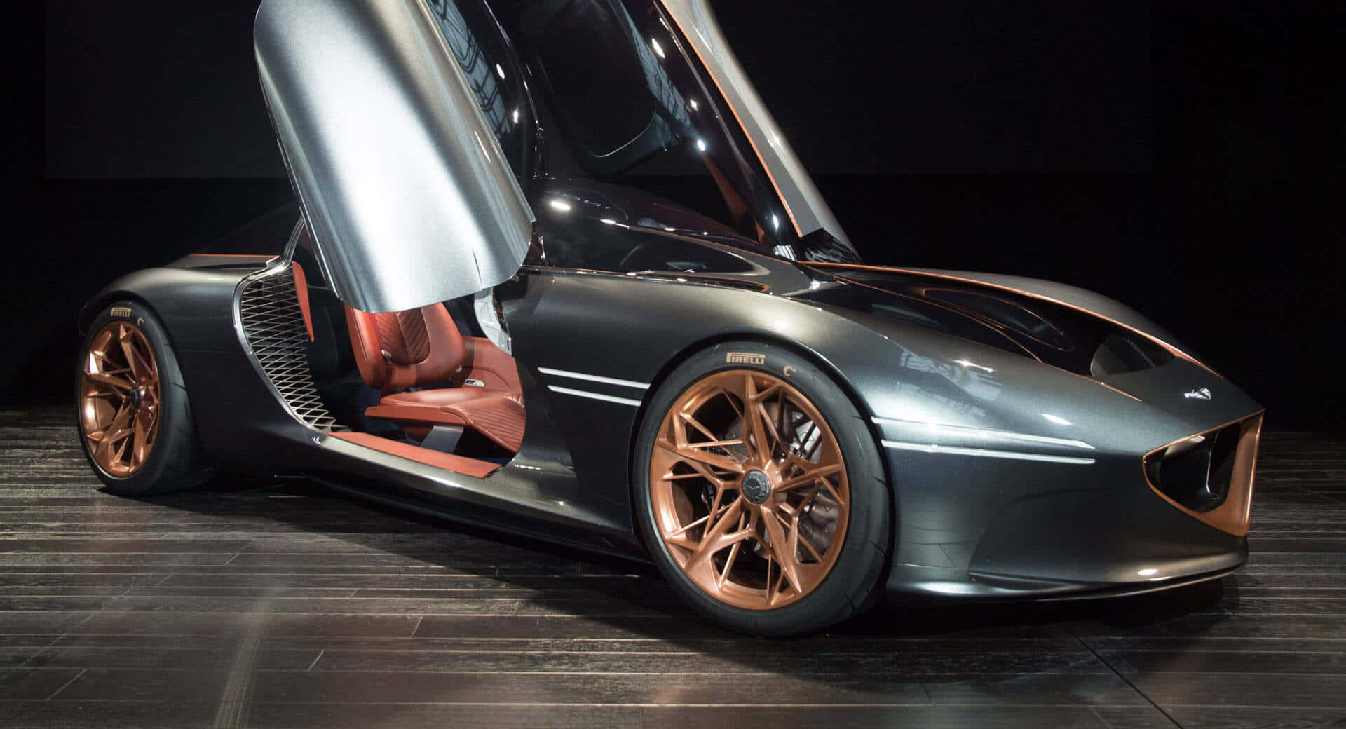 Genesis Essentia 桌布 壁紙 — 一輛時尚的未來主義跑車，配備鷗翼門和銅色點綴，在深色木地板上於攝影棚燈光下閃閃發光。
