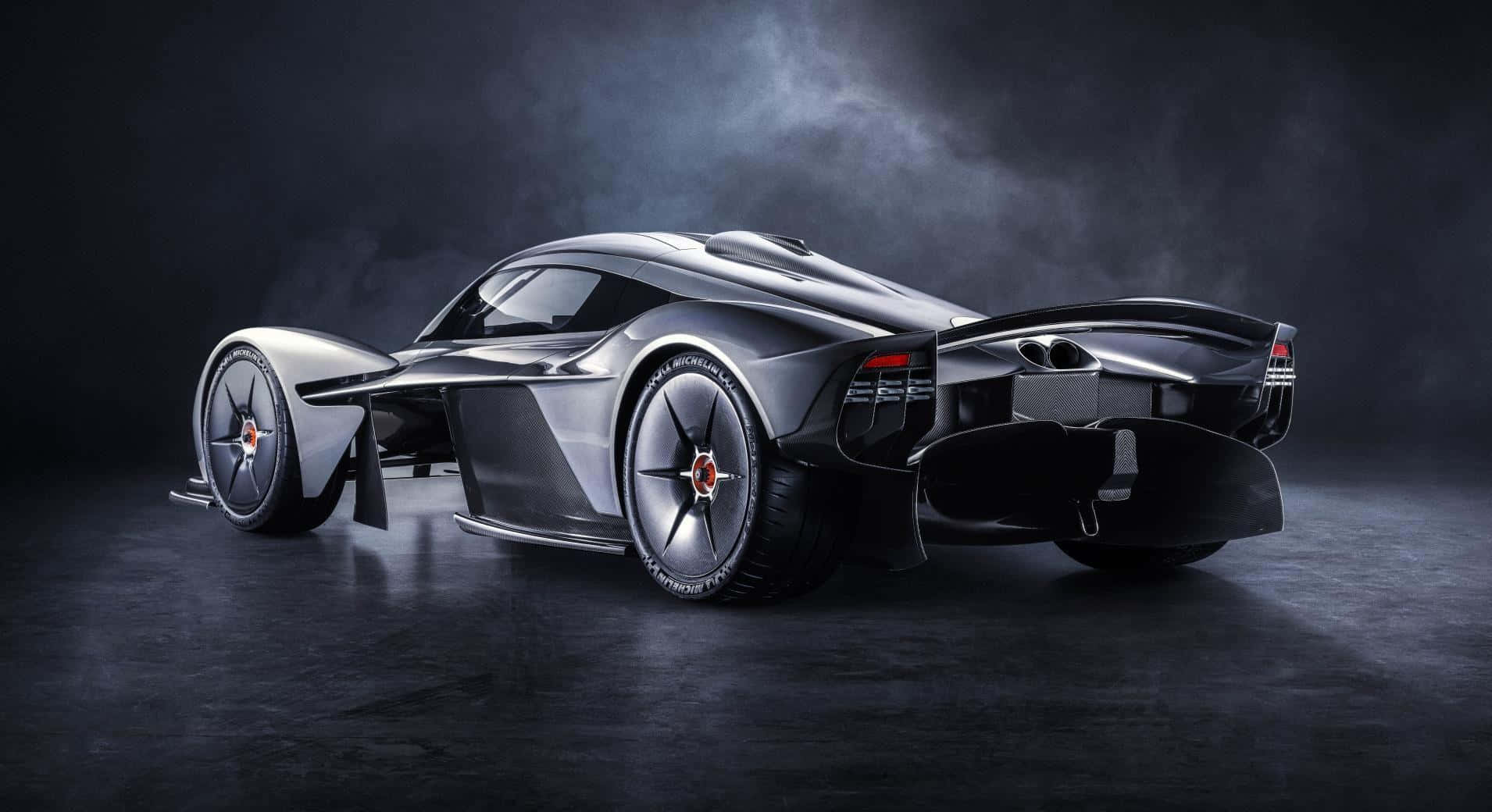 Aston Martin Valkyrie 桌布 壁紙 — 一輛時尚的未來感銀色跑車，配備外露車輪和空氣動力學設計，在戲劇性的工作室燈光下閃耀。