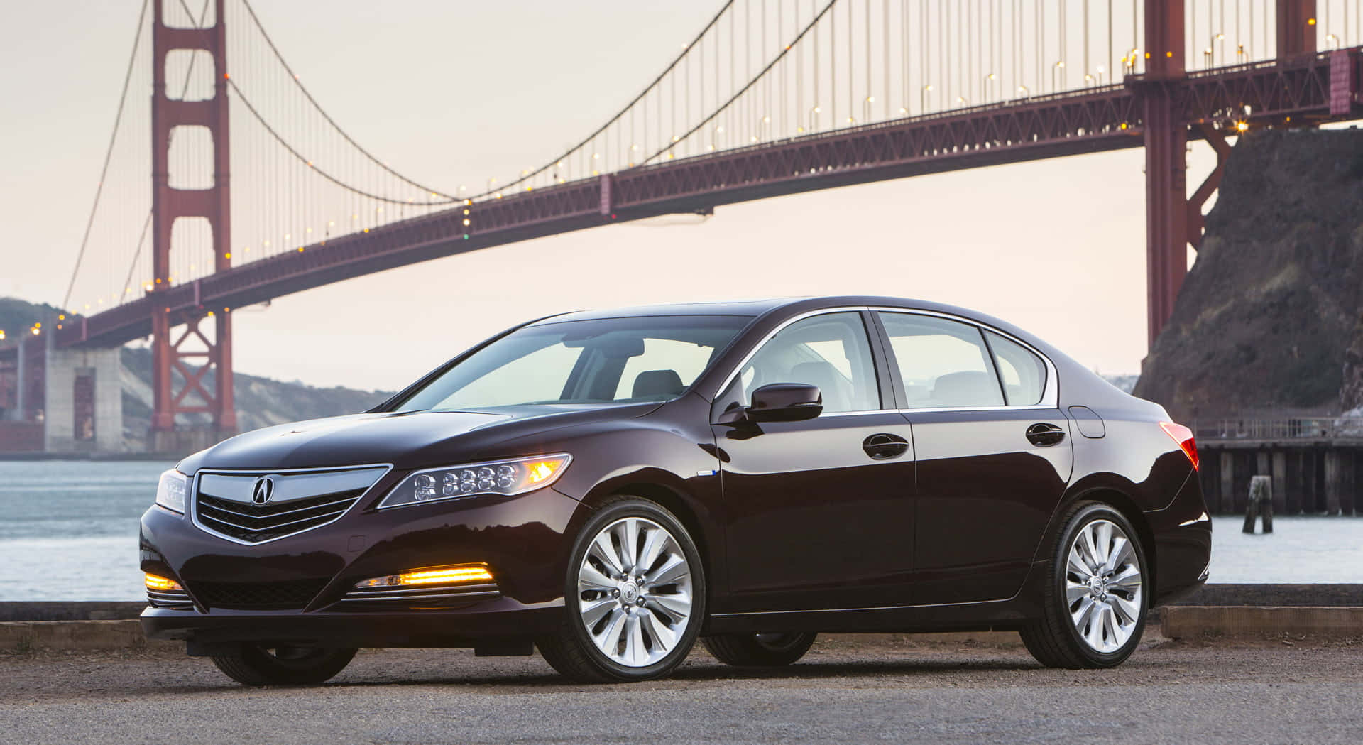 Acura Rlx 桌布 壁紙 — 一輛時尚的栗色轎車停在水邊，背景中標誌性的金門大橋在黃昏時分柔和地發光。