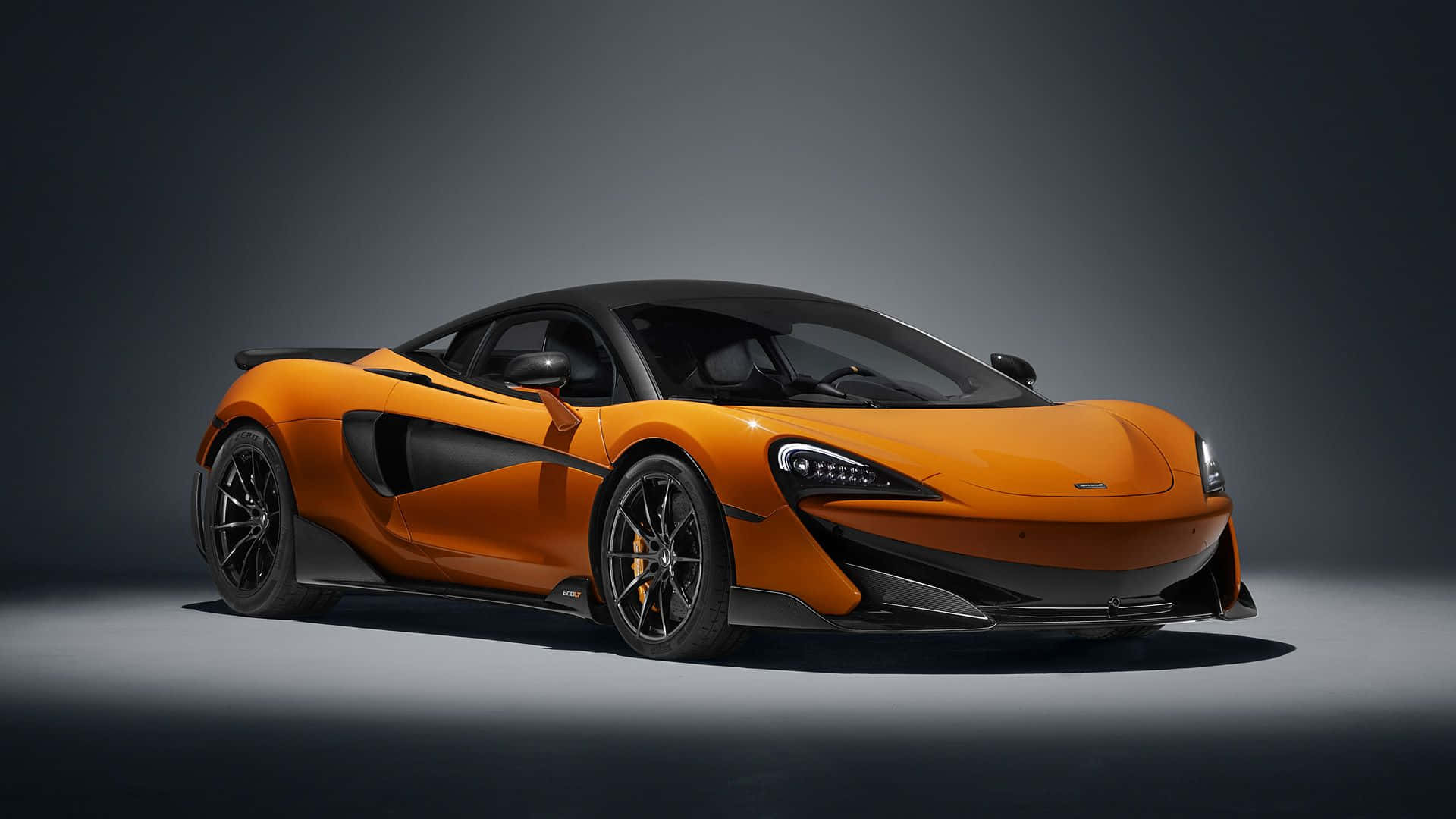 Mclaren 600lt 桌布 壁紙 — 一輛時尚的橙色McLaren跑車，帶有黑色飾件，在戲劇性燈光的攝影棚中展示。