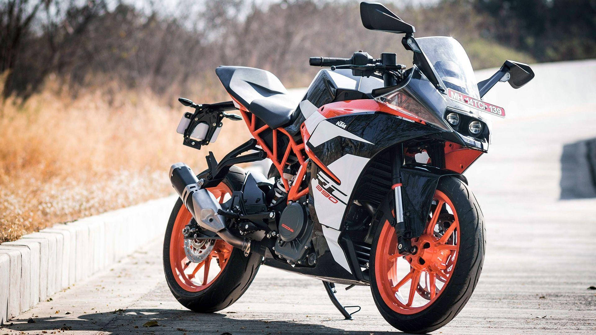 機車 桌布 壁紙 — 一輛時尚的橙色和黑色KTM RC 390電單車停在路邊，有乾草和混凝土路緣，在明亮的陽光下。