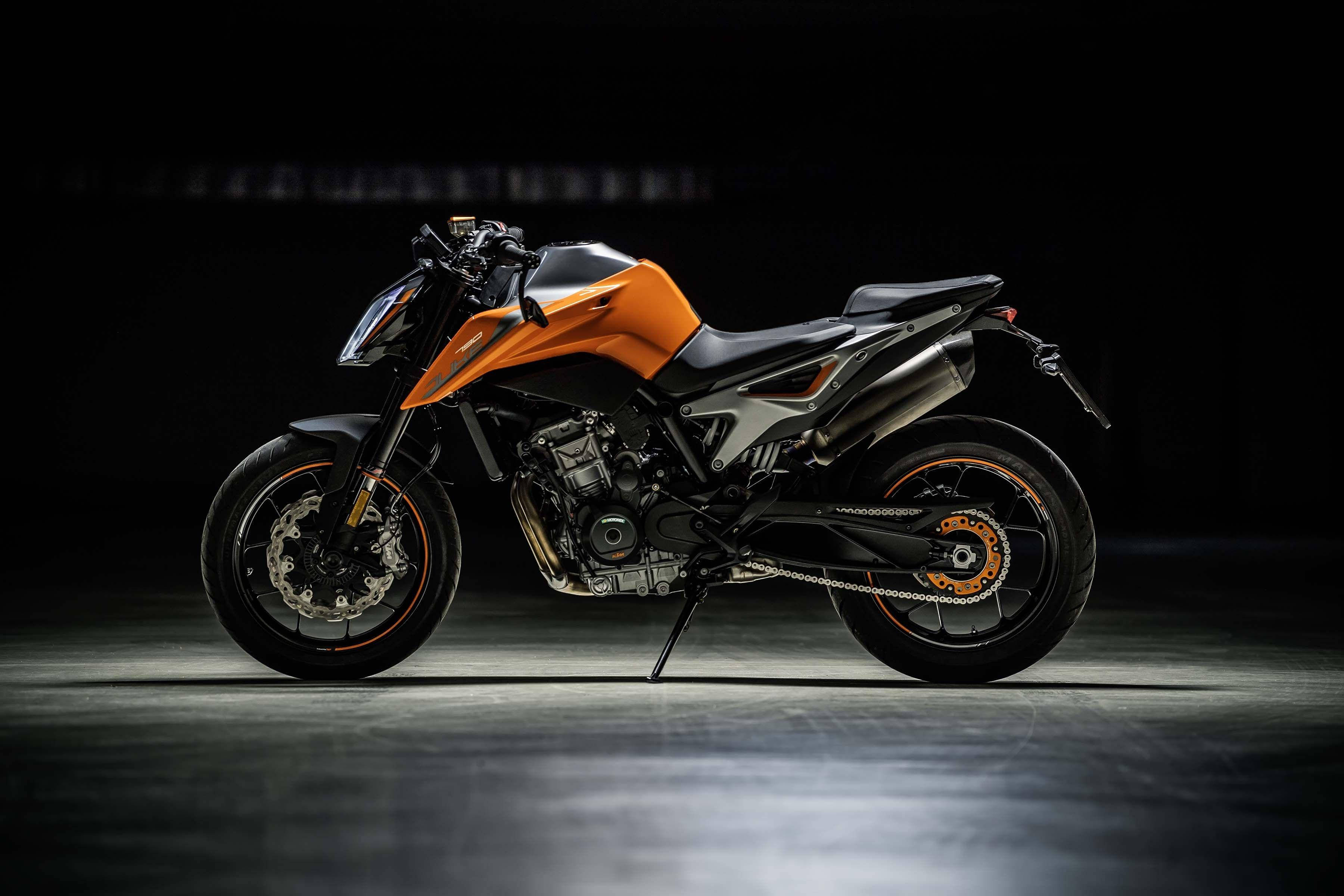 ktm bikes 桌布 壁紙 — 一輛時尚的橙色和黑色運動摩托車在黑暗的攝影棚地板上，被聚光燈反射戲劇性地照亮。