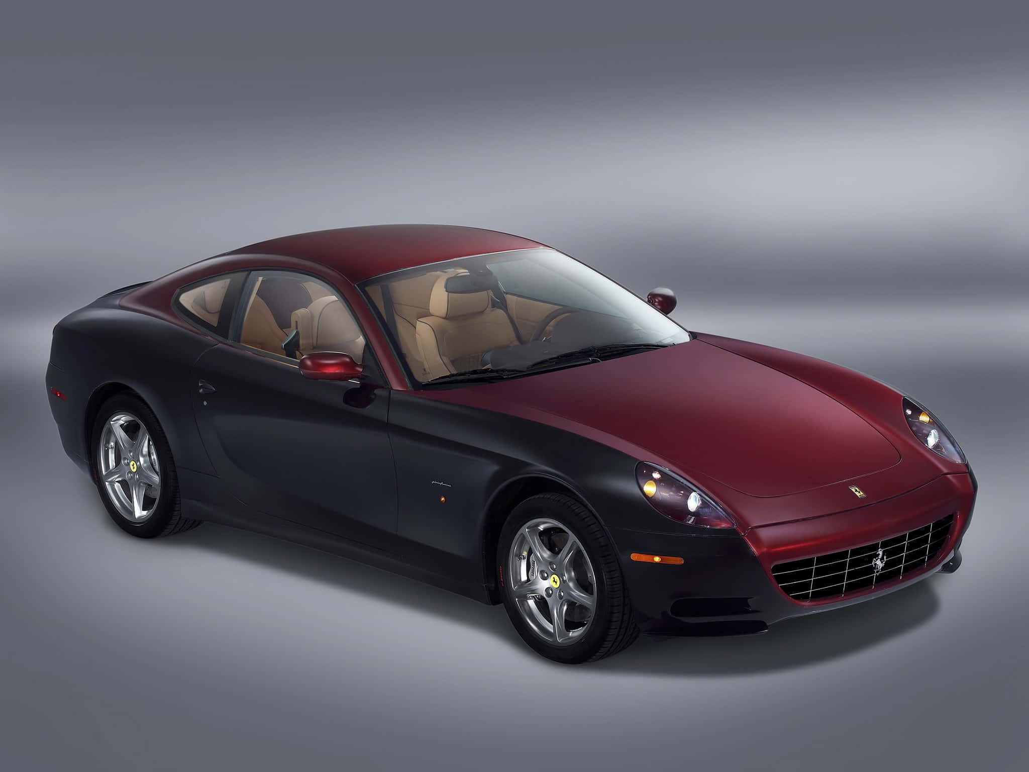 Ferrari 612 Scaglietti 桌布 壁紙 — 一輛時尚的法拉利雙門跑車，擁有紅黑雙色車身和米色皮革內飾，在漸變灰色工作室背景前擺拍。