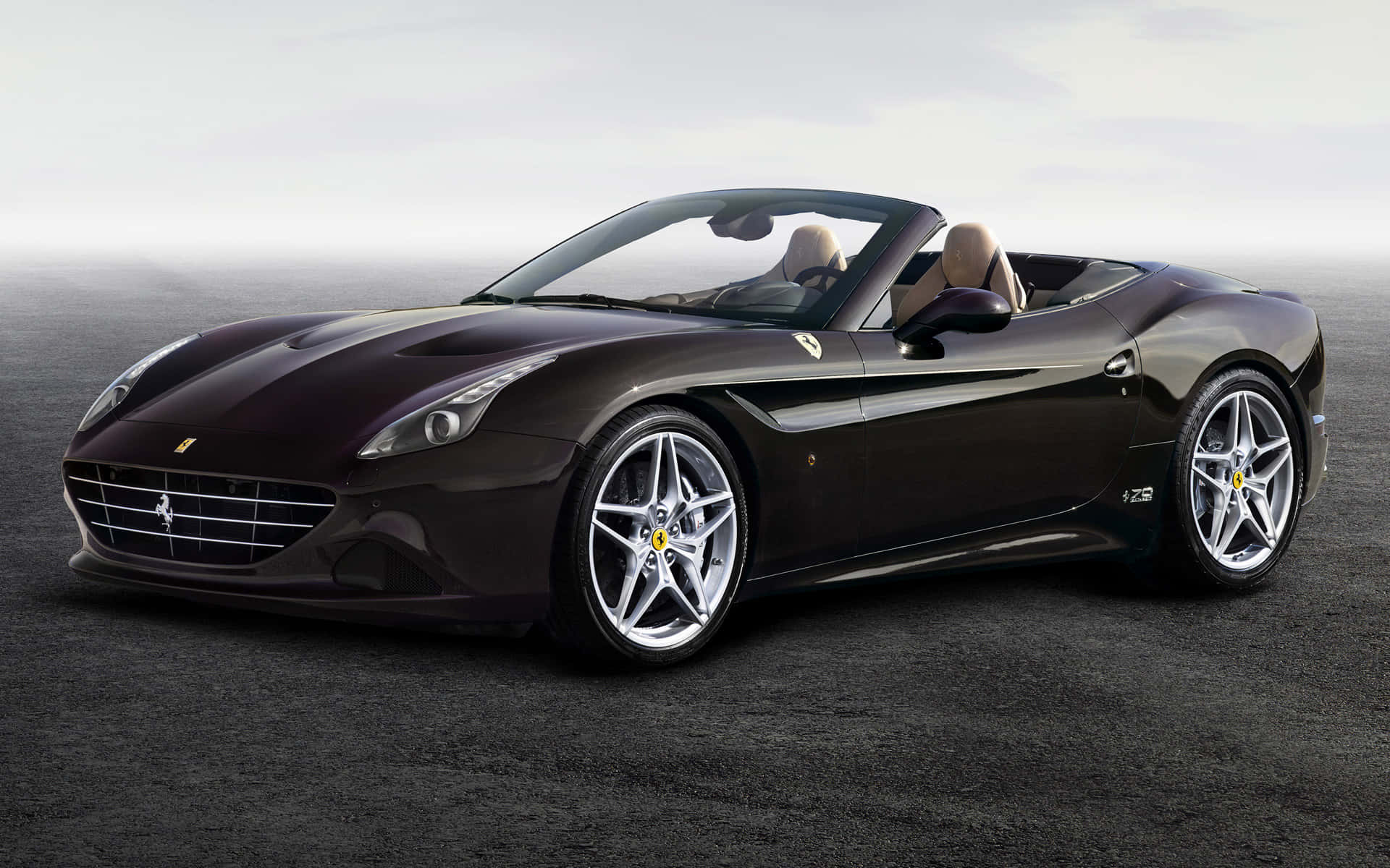 Ferrari California T 桌布 壁紙 — 一輛時尚的深棕色法拉利敞篷車配備銀色輪圈，在柔和的日光下停放在霧濛濛的灰色瀝青路面上。