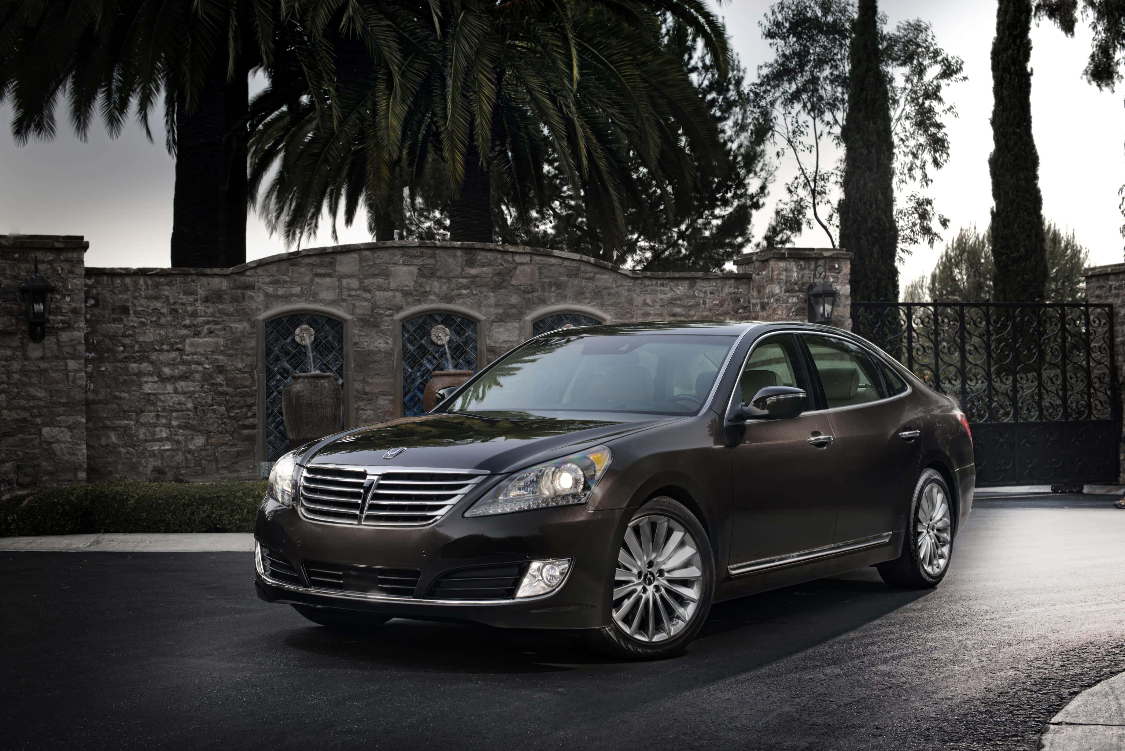 Hyundai Equus 桌布 壁紙 — 一輛時尚的深棕色豪華轎車停在車道上，前面是石牆，有棕櫚樹和拱形窗戶。
