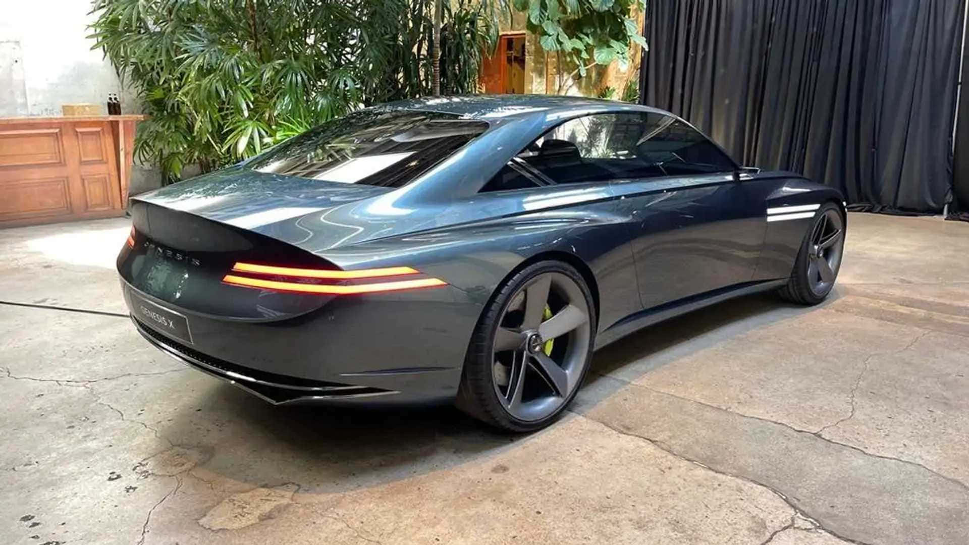Genesis X Concept 桌布 壁紙 — 一輛時尚的深灰色 Genesis 跑車，帶有發光的尾燈，停在室內，旁邊是茂盛的綠色植物。