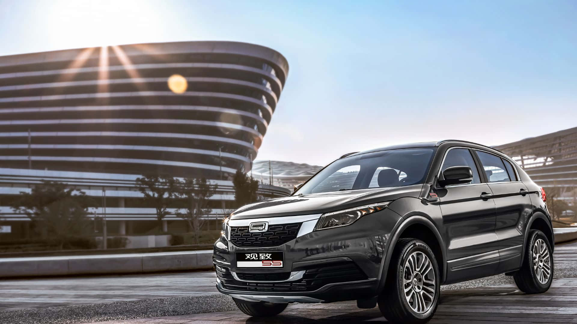 Qoros 桌布 壁紙 — 一輛時尚的深灰色SUV停在一棟現代弧形建築前，陽光穿透天空。