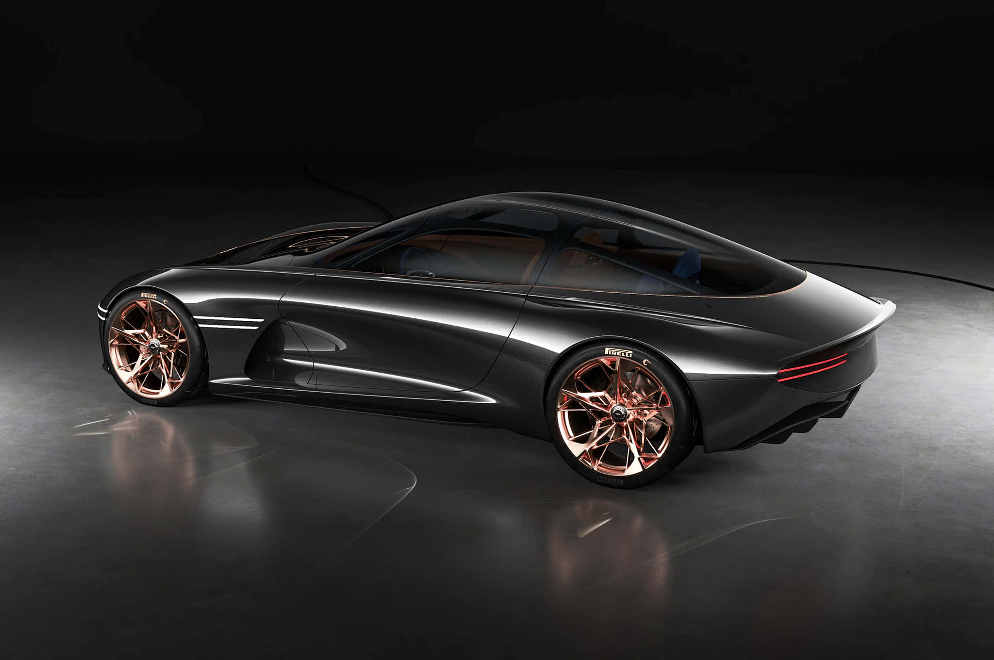 Genesis Essentia 桌布 壁紙 — 一輛時尚的深灰色概念車，配備銅色輪轂，在攝影棚燈光下於反光地板上閃耀。