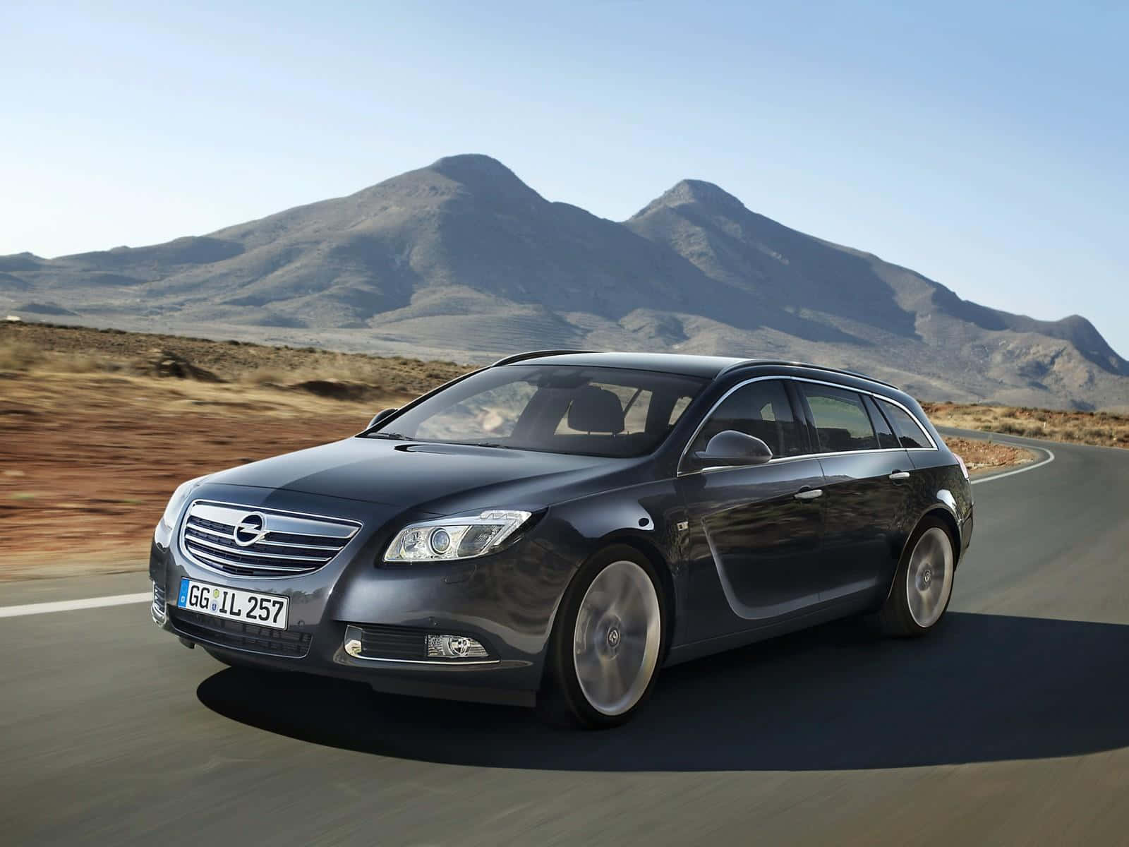 Opel Insignia 桌布 壁紙 — 一輛時尚的深灰色歐寶Insignia旅行車在晴朗的藍天下沿著蜿蜒的山路行駛。
