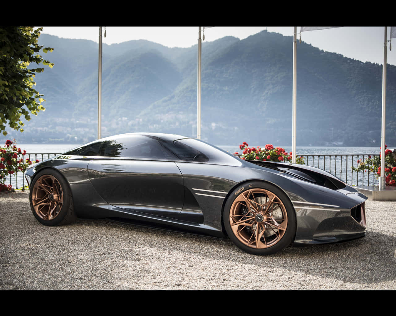 Genesis Essentia 桌布 壁紙 — 一輛時尚的深灰色跑車配青銅輪圈，停在湖邊的碎石地上，背景有山巒。