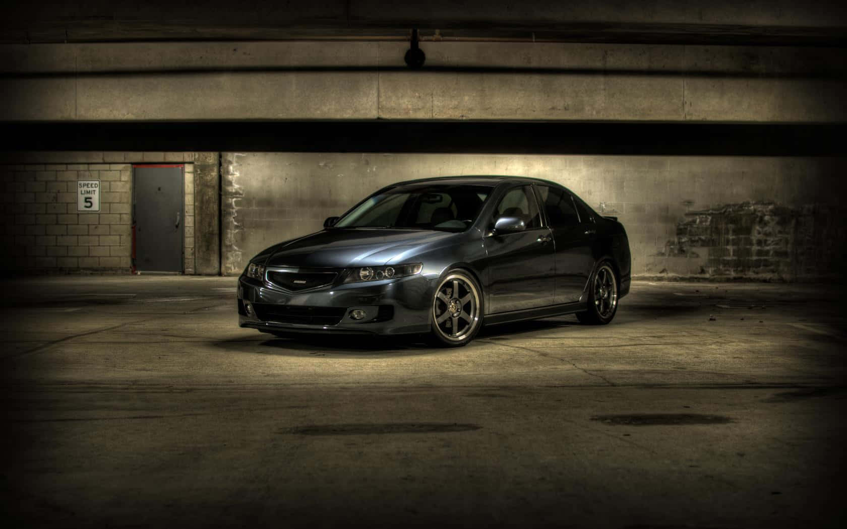 Acura Tsx 桌布 壁紙 — 一輛時尚的深灰色轎車停在昏暗的混凝土車庫燈光下，帶有戲劇性的陰影。