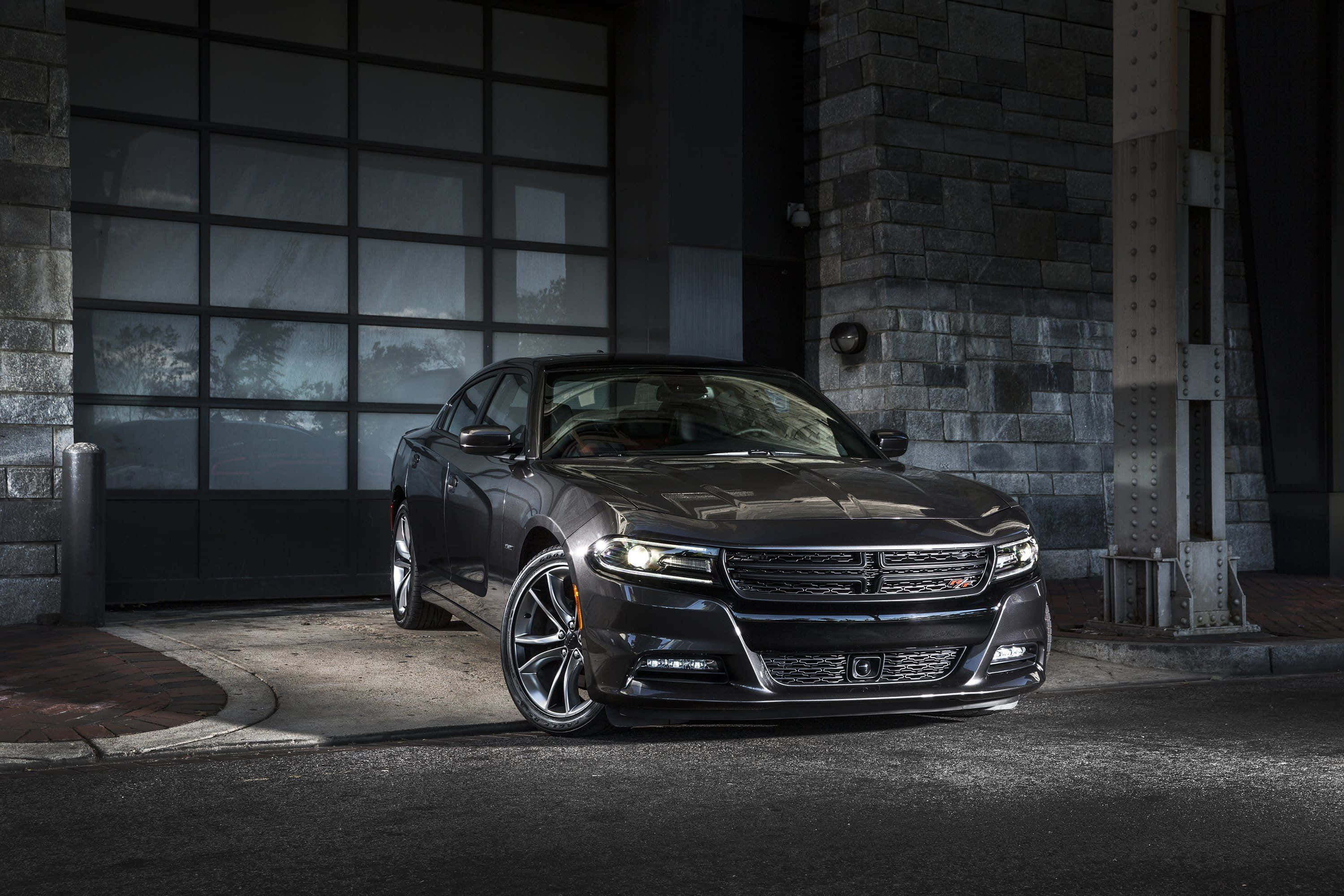 Dodge Charger 桌布 壁紙 — 一輛時尚的深灰色道奇Charger在夜間停在一棟帶有大型玻璃車庫門的石頭建築前。