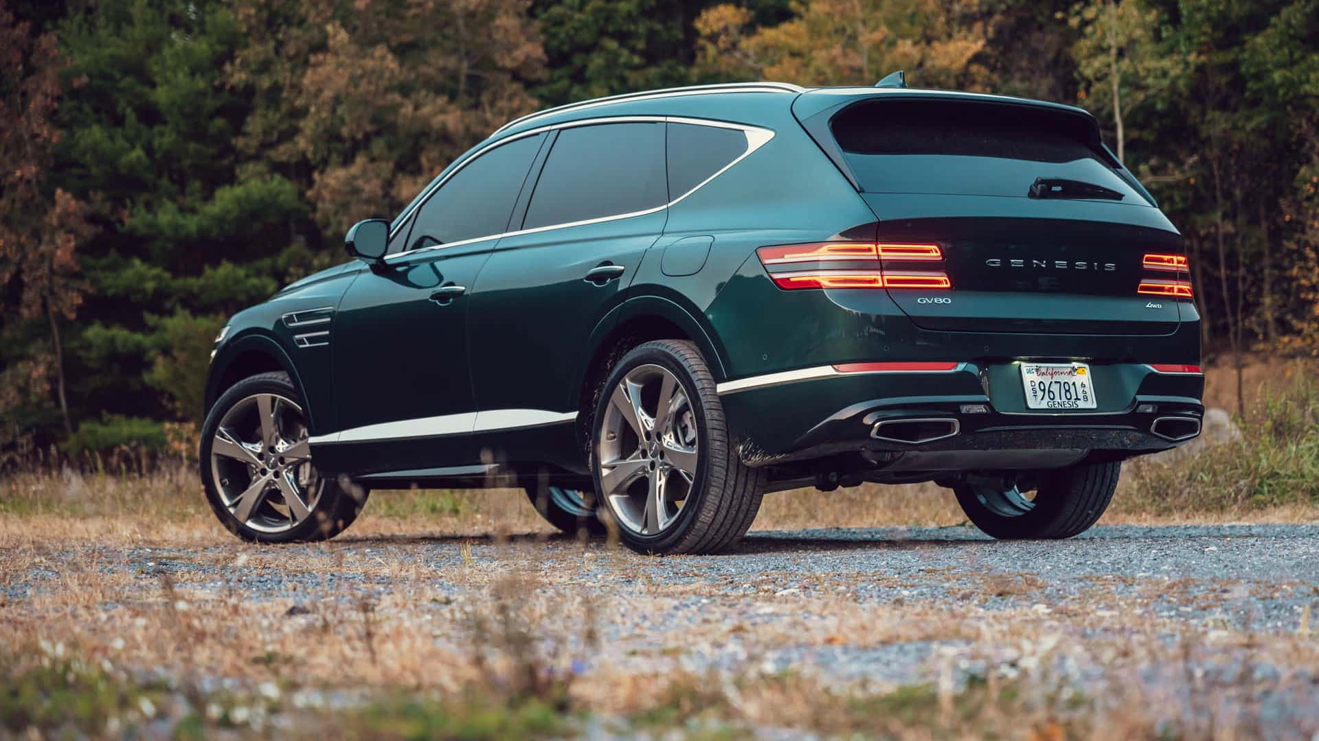 Genesis Gv80 桌布 壁紙 — 一輛時尚的深綠色 Genesis GV80 SUV 停泊在鋪滿碎石的小徑上，周圍環繞著秋樹。