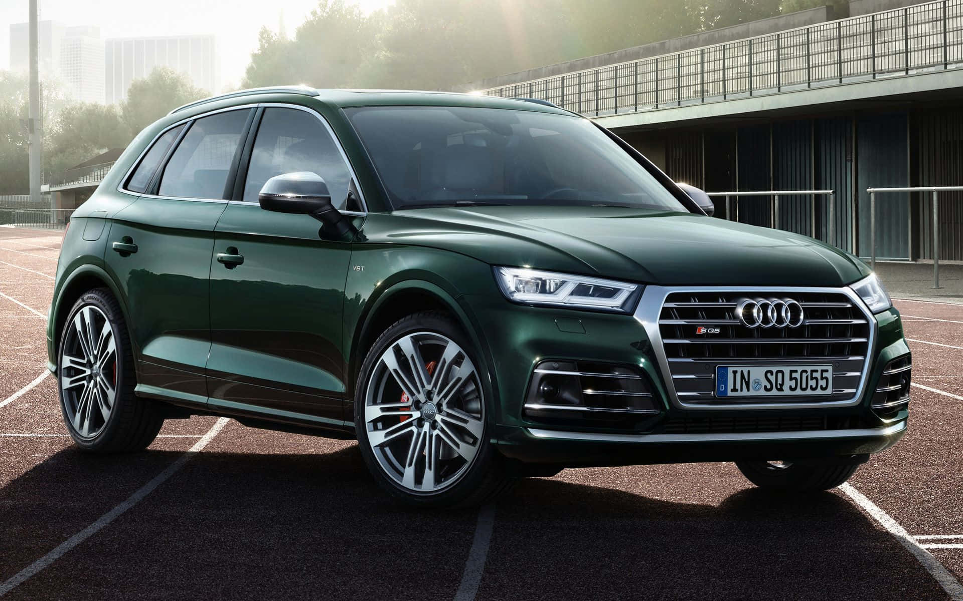 Audi Sq5 桌布 壁紙 — 一輛時尚的深綠色Audi SQ5 SUV停泊在陽光普照的網球場上，背景是現代建築。