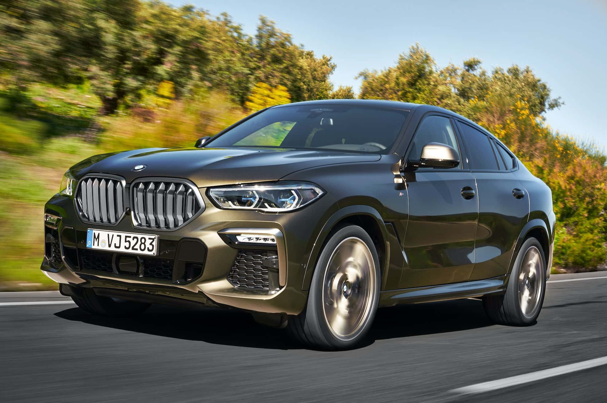 Bmw X6 桌布 壁紙 — 一輛時尚的深綠色BMW X6 SUV在陽光明媚的道路上行駛，背景是模糊的秋樹。