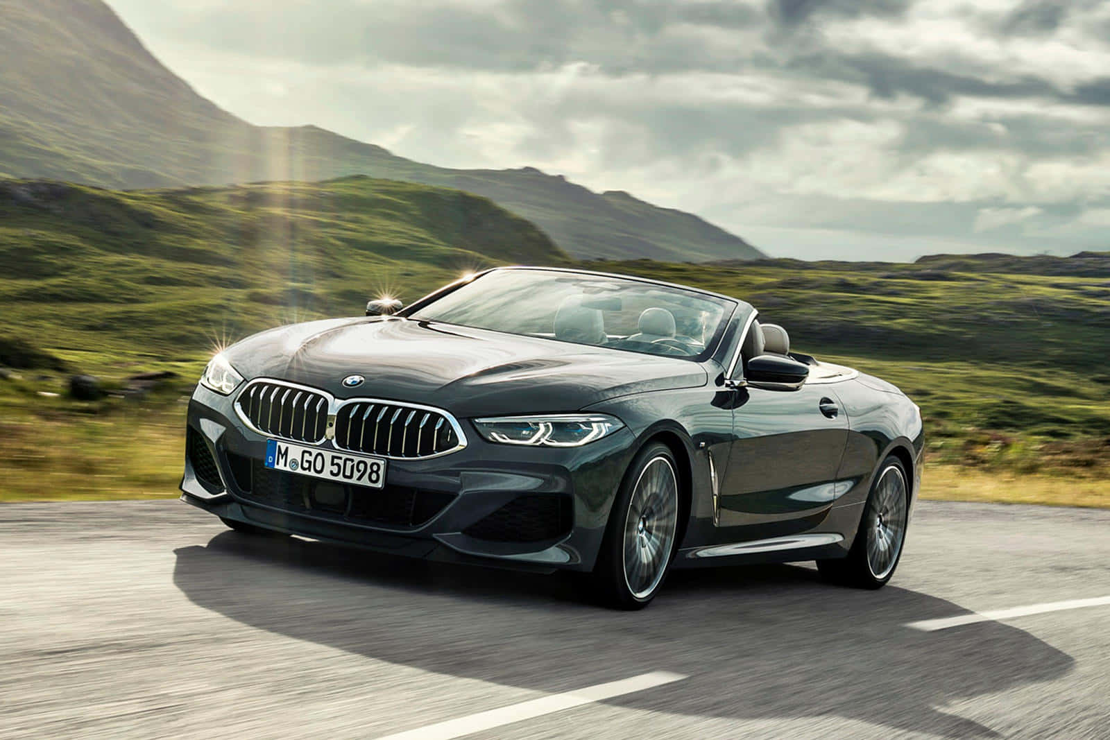 Bmw 8 Series 桌布 壁紙 — 一輛時尚的深綠色BMW開篷車在陰天下行駛在蜿蜒的山路上。