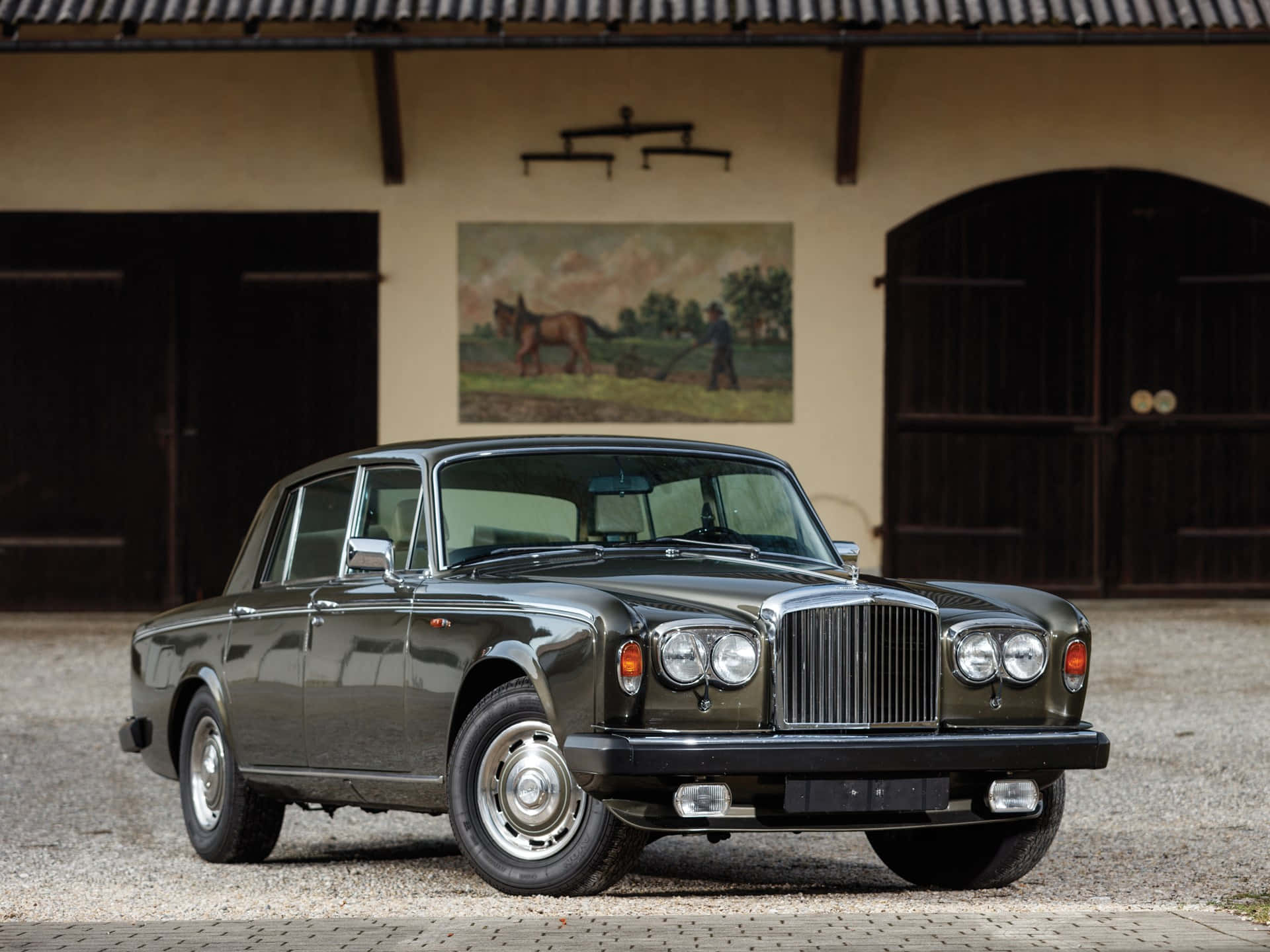 Bentley T2 桌布 壁紙 — 一輛時尚的深綠色復古賓利轎車停在碎石路上，前方是質樸的穀倉，門上方有馬匹畫作。