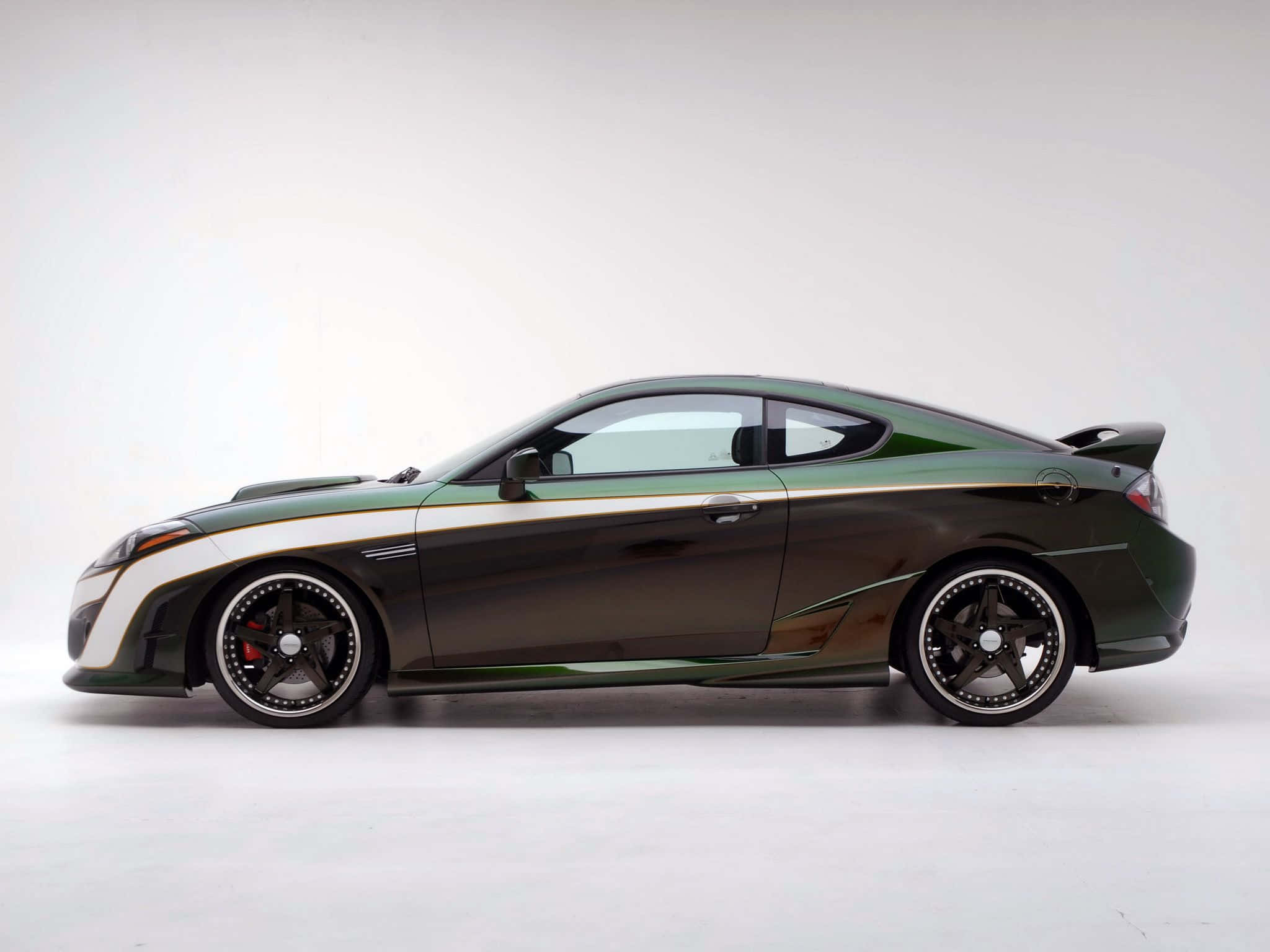 Hyundai Tiburon 桌布 壁紙 — 一輛時尚的深綠色跑車，帶有白色點綴和黑色輪圈，矗立在簡約的工作室環境中。