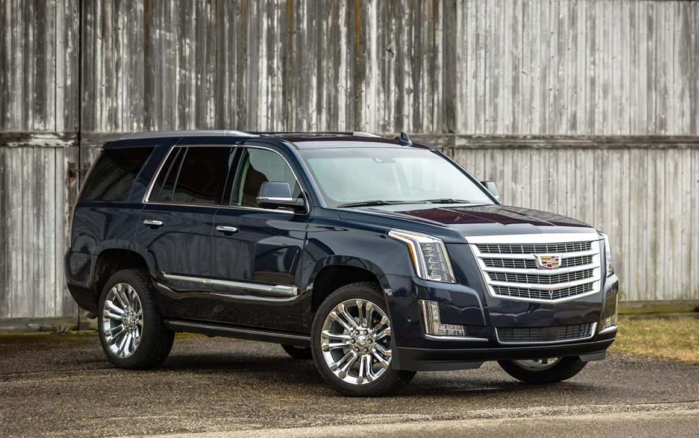 Cadillac Escalade 桌布 壁紙 — 一輛時尚的深藍色 Cadillac SUV 停在風化的木製穀倉前，配備反光鍍鉻輪圈。