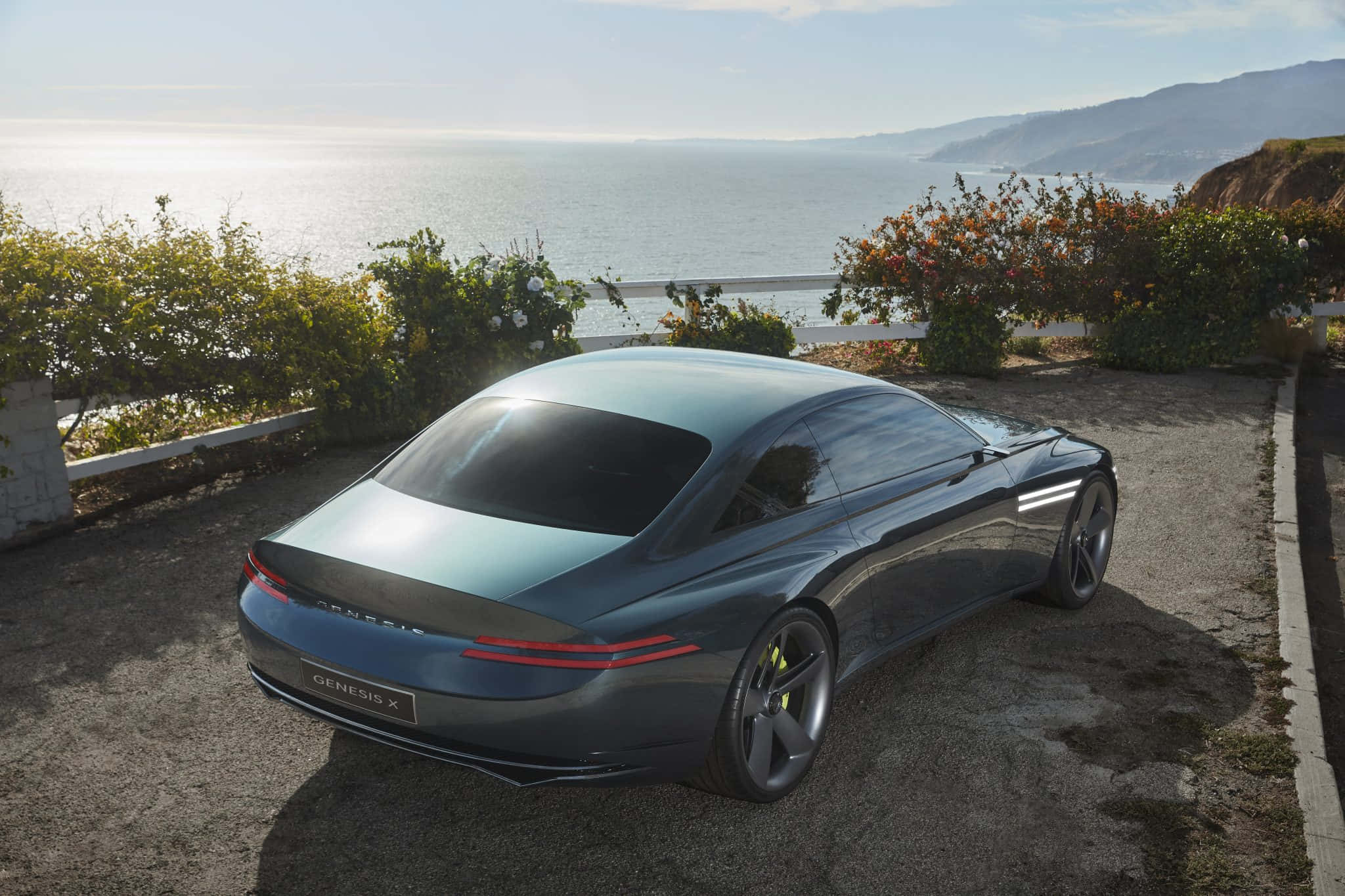 Genesis X Concept 桌布 壁紙 — 一輛時尚的深藍色 Genesis X 概念車停泊在俯瞰海洋的海岸懸崖上，遠方有陽光普照的山丘。