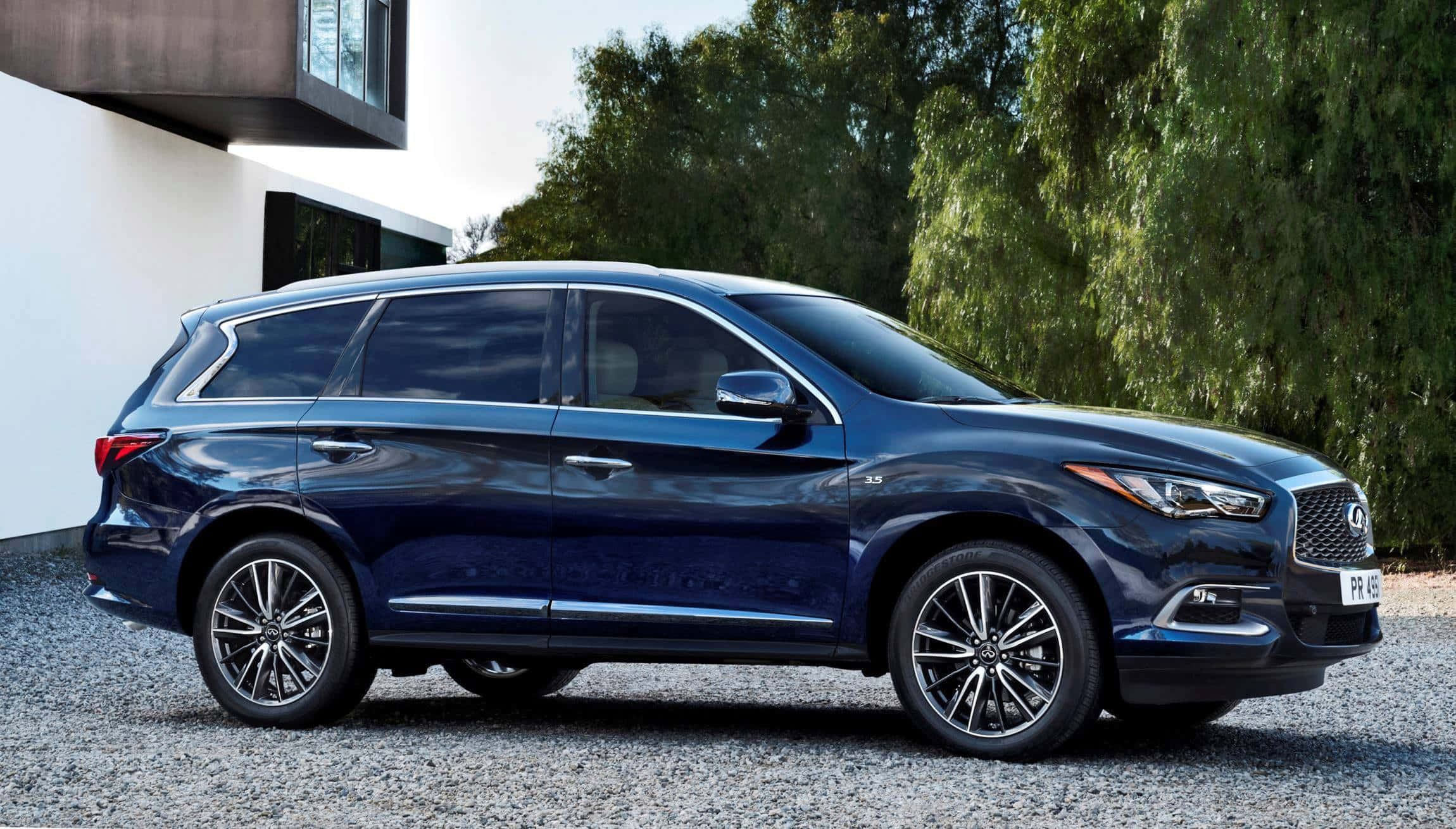 Infiniti Qx60 桌布 壁紙 — 一輛時尚的深藍色 Infiniti QX60 SUV 停放在碎石路上，旁邊是一座現代白色房屋，背景是茂密的綠樹。